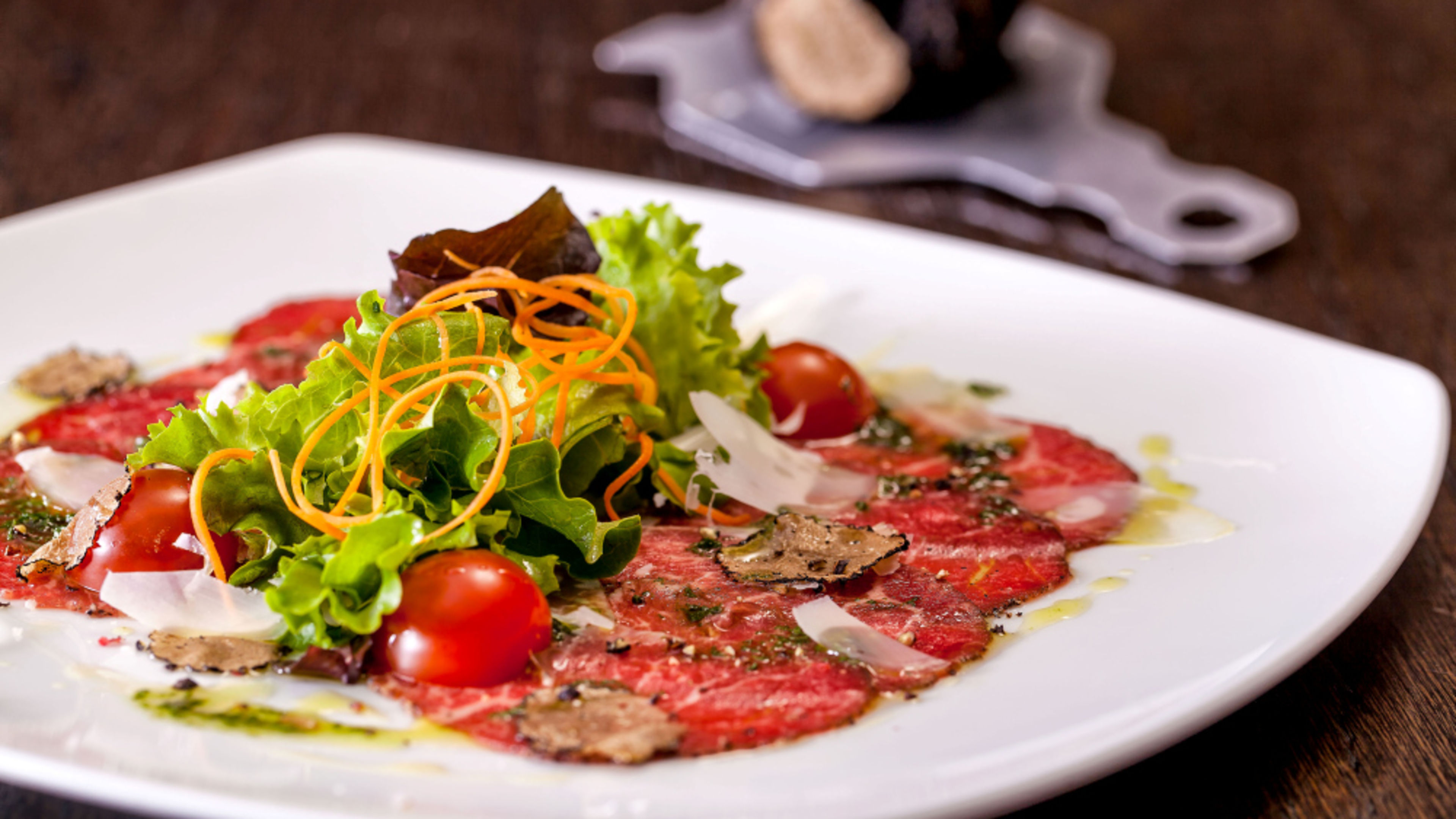 Rindfleisch-Carpaccio mit Trüffel, Kirschtomaten und frischem Salat auf weißem Teller. Rindfleisch-Carpaccio mit Trüffel, Kirschtomaten und frischem Salat auf weißem Teller.