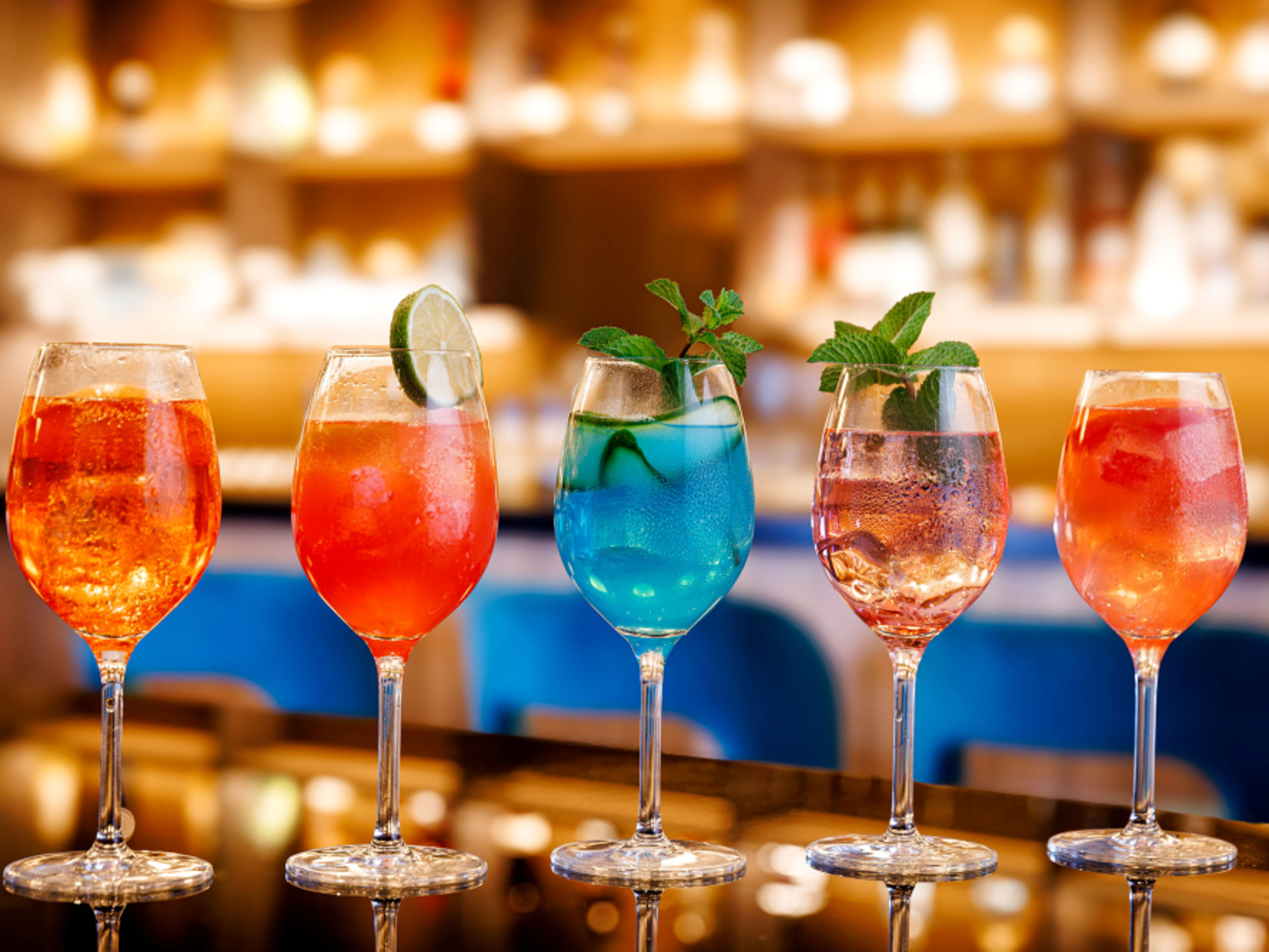 Five colourful Sprizz cocktails in wine glasses, garnished with lime and mint, at a bar. Five colourful Sprizz cocktails in wine glasses, garnished with lime and mint, at a bar.