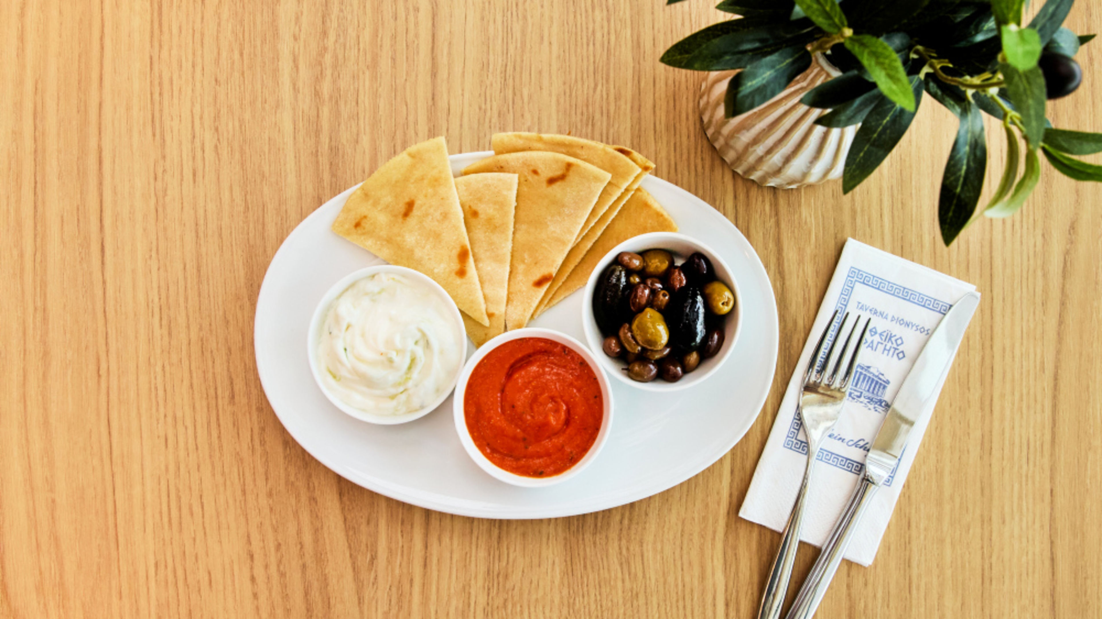 Pita bread with tzatziki, red dip and olives on a wooden table, with cutlery beside it Pita bread with tzatziki, red dip and olives on a wooden table, with cutlery beside it