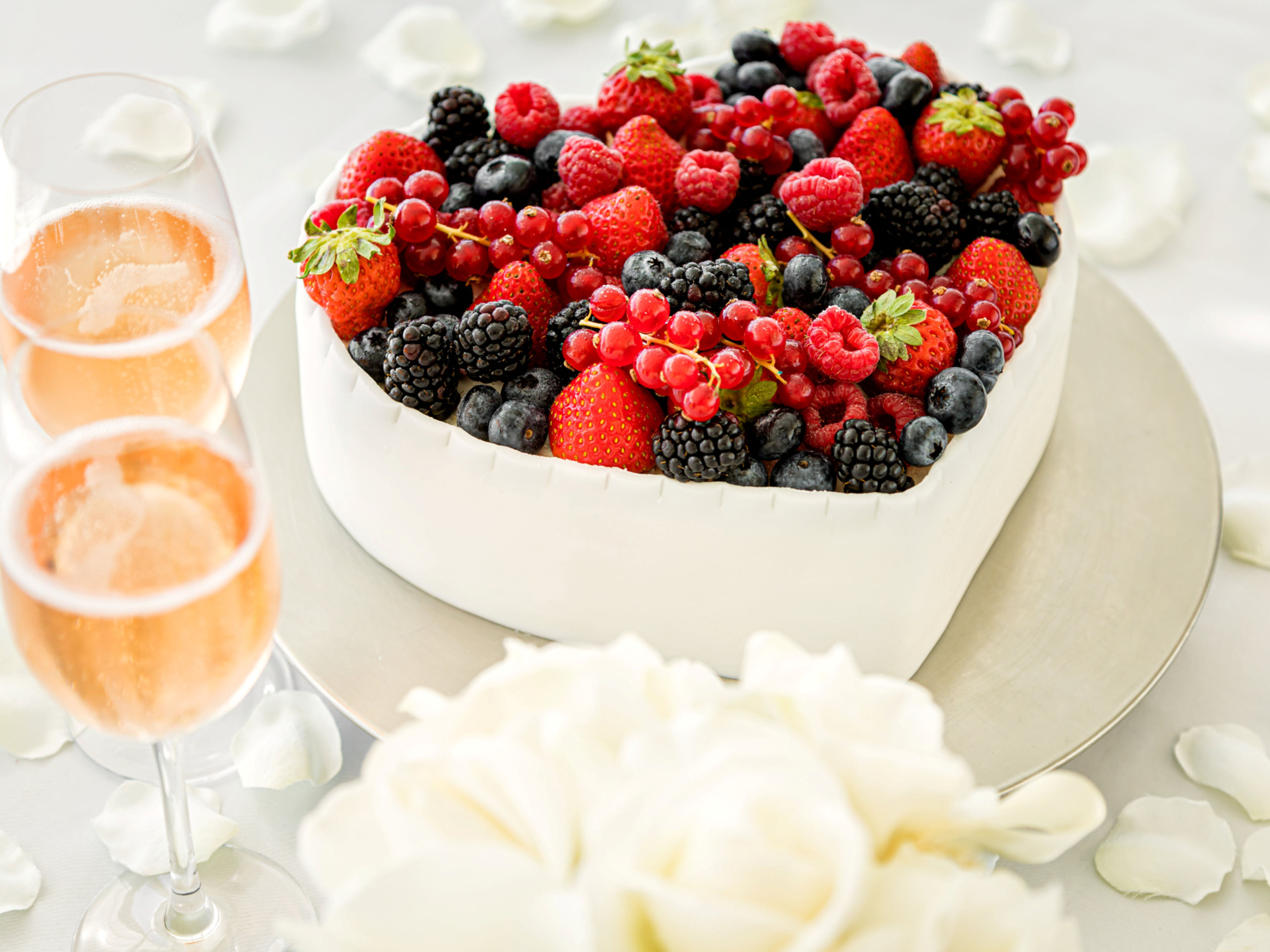 Herzförmige Beerenkuchen mit Sektgläsern und weißen Rosenblättern. Herzförmige Beerenkuchen mit Sektgläsern und weißen Rosenblättern.