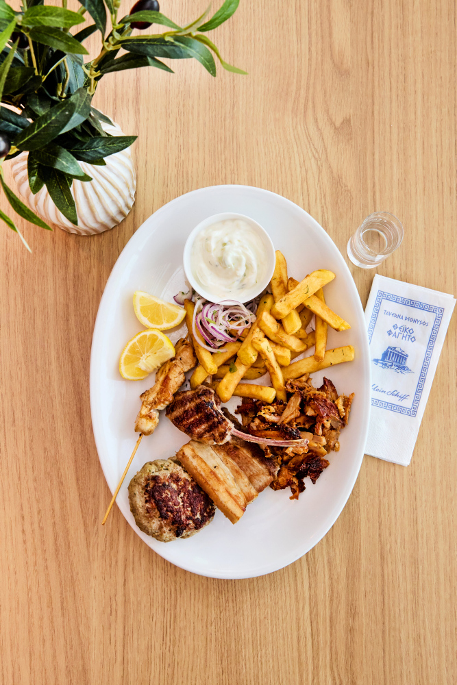 Greek barbecue platter with chips, tzatziki, lemon and onions on a wooden table