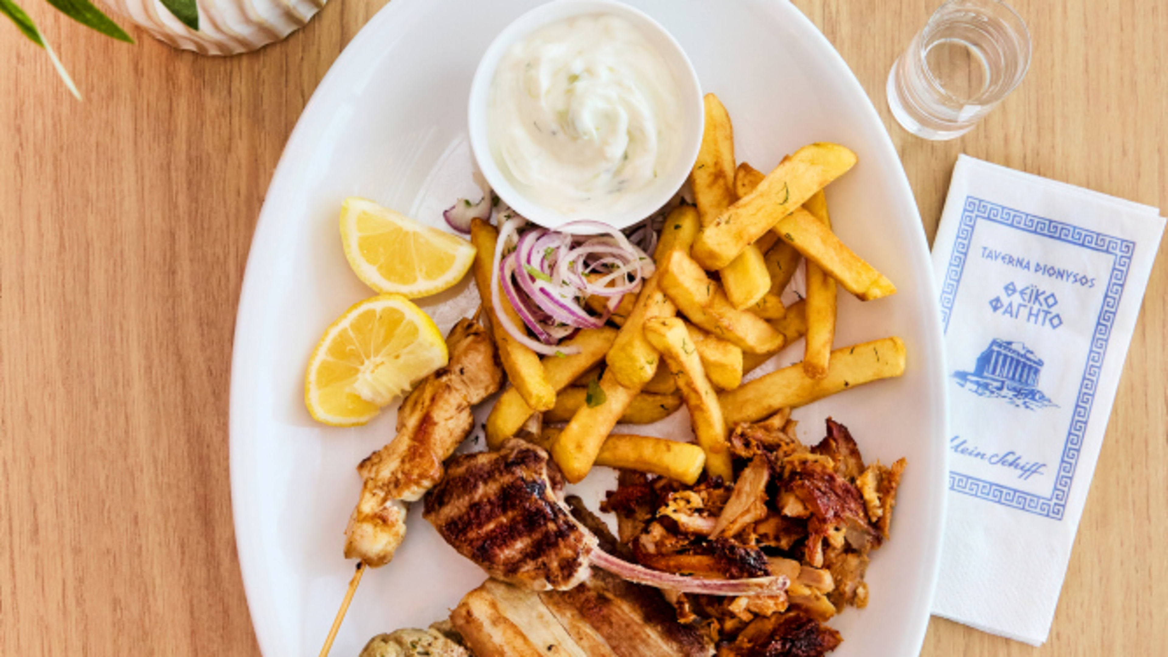 Greek barbecue platter with chips, tzatziki, lemon and onions on a wooden table Greek barbecue platter with chips, tzatziki, lemon and onions on a wooden table