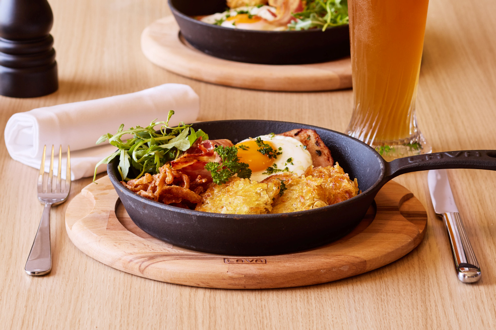 Rösti mit Spiegelei und Speck, serviert in einer schwarzen Pfanne.