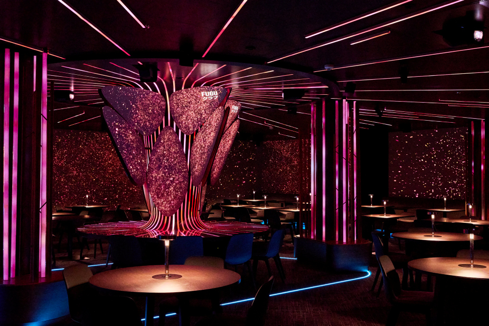 FUGU-Lounge mit runden Esstischen, beleuchtet durch pinkes Licht, das in Säulen integriert ist.