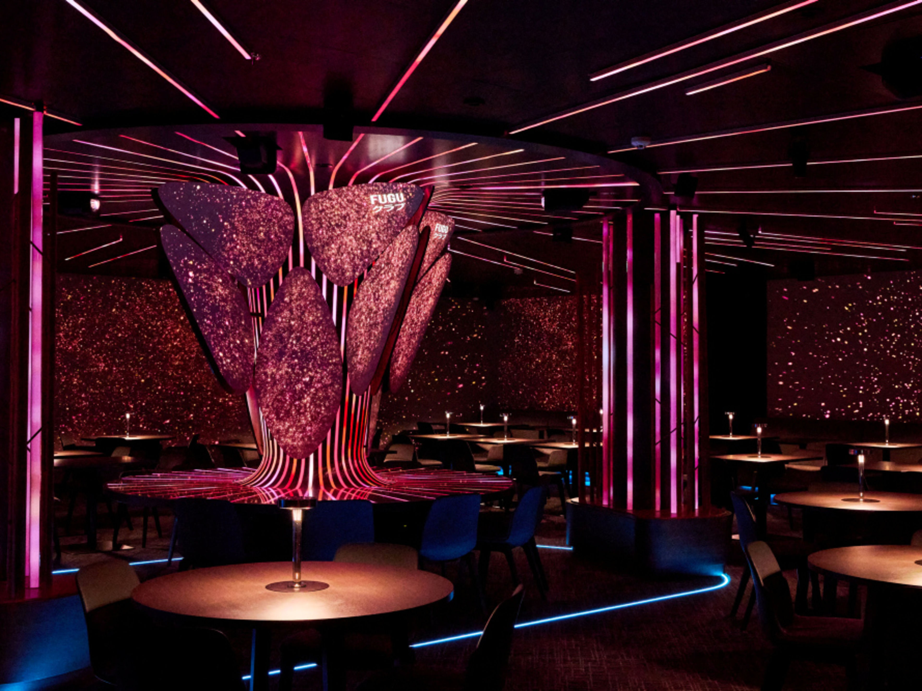 FUGU lounge with round dining tables, illuminated by pink light integrated into columns. FUGU lounge with round dining tables, illuminated by pink light integrated into columns.