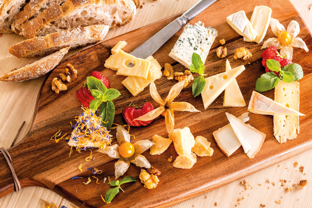 A cheese platter with bread, nuts, strawberries and mint.