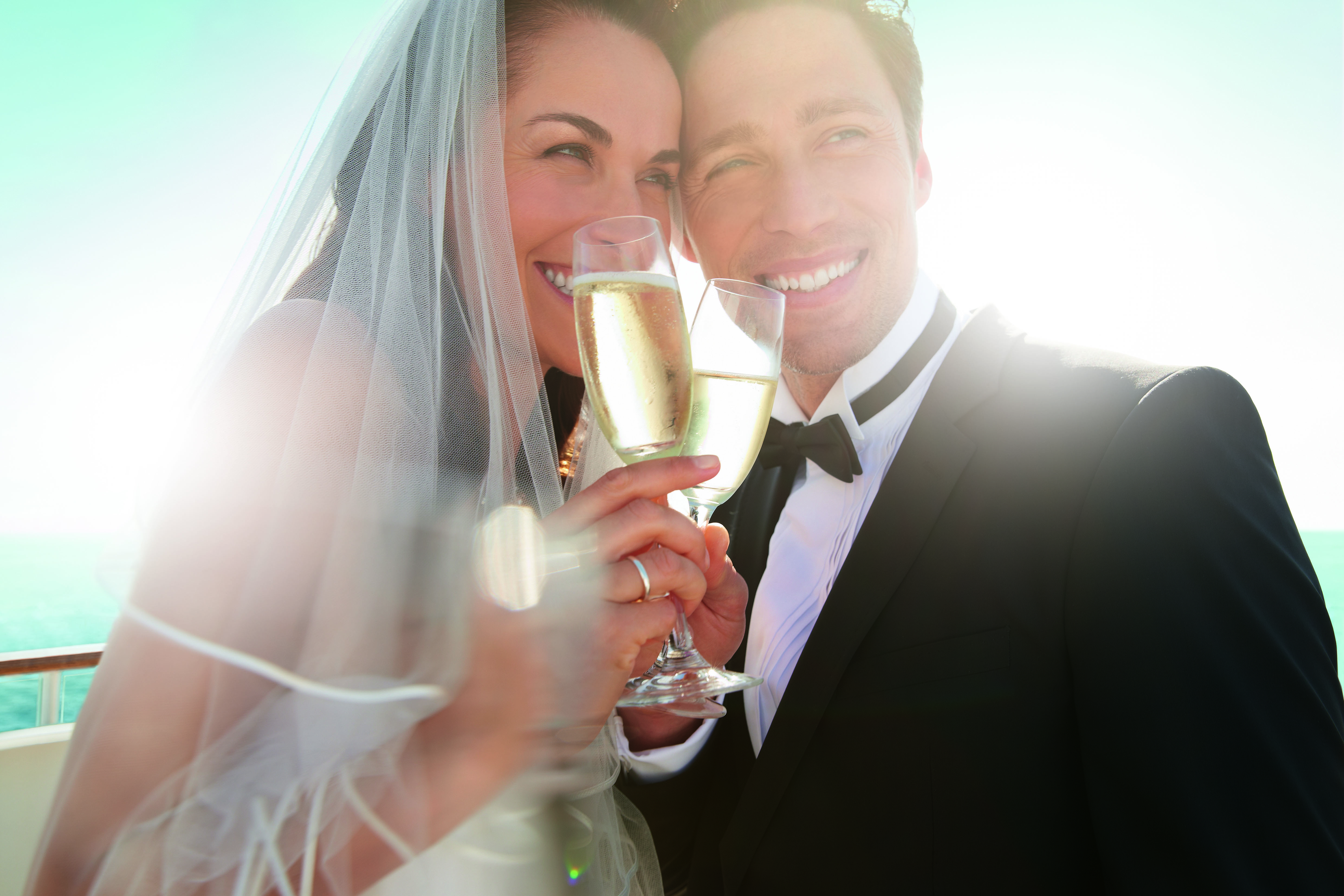 Bride and groom toasting with champagne, sunny day, sea background.