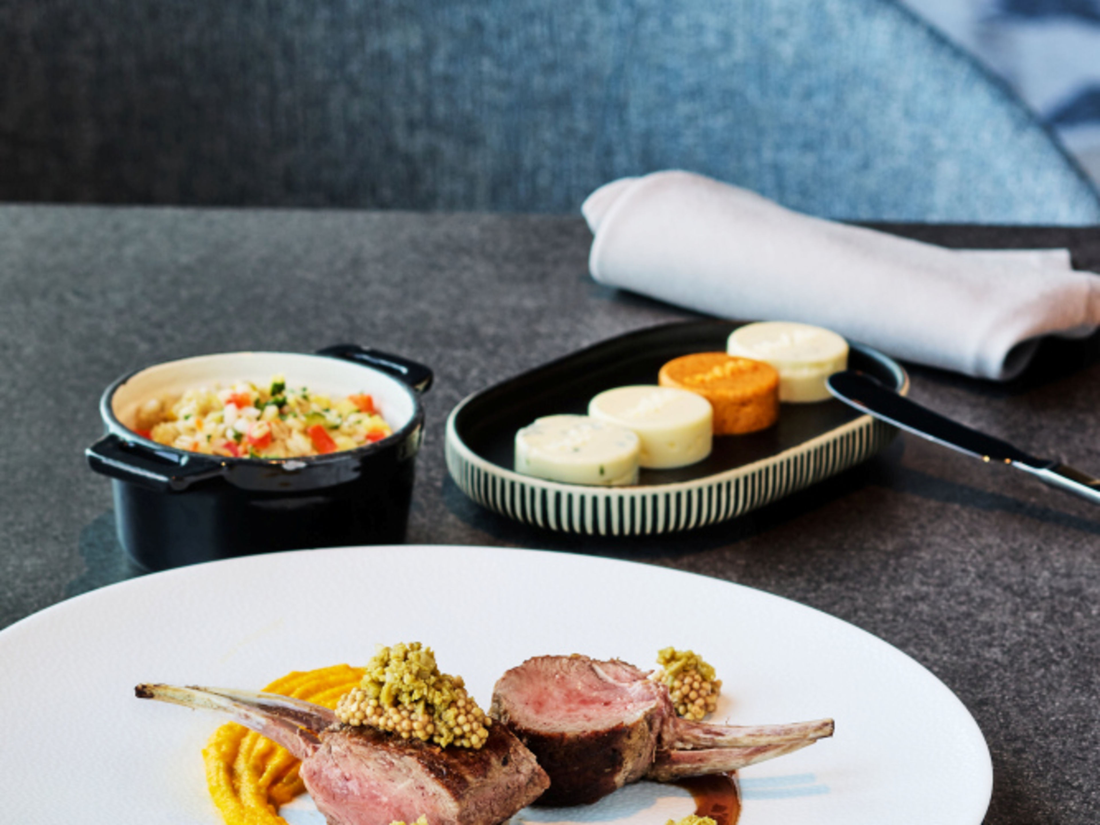 Lammkarree mit Senfkruste, Gemüsebeilage und Käse auf grauem Tisch. Lammkarree mit Senfkruste, Gemüsebeilage und Käse auf grauem Tisch.