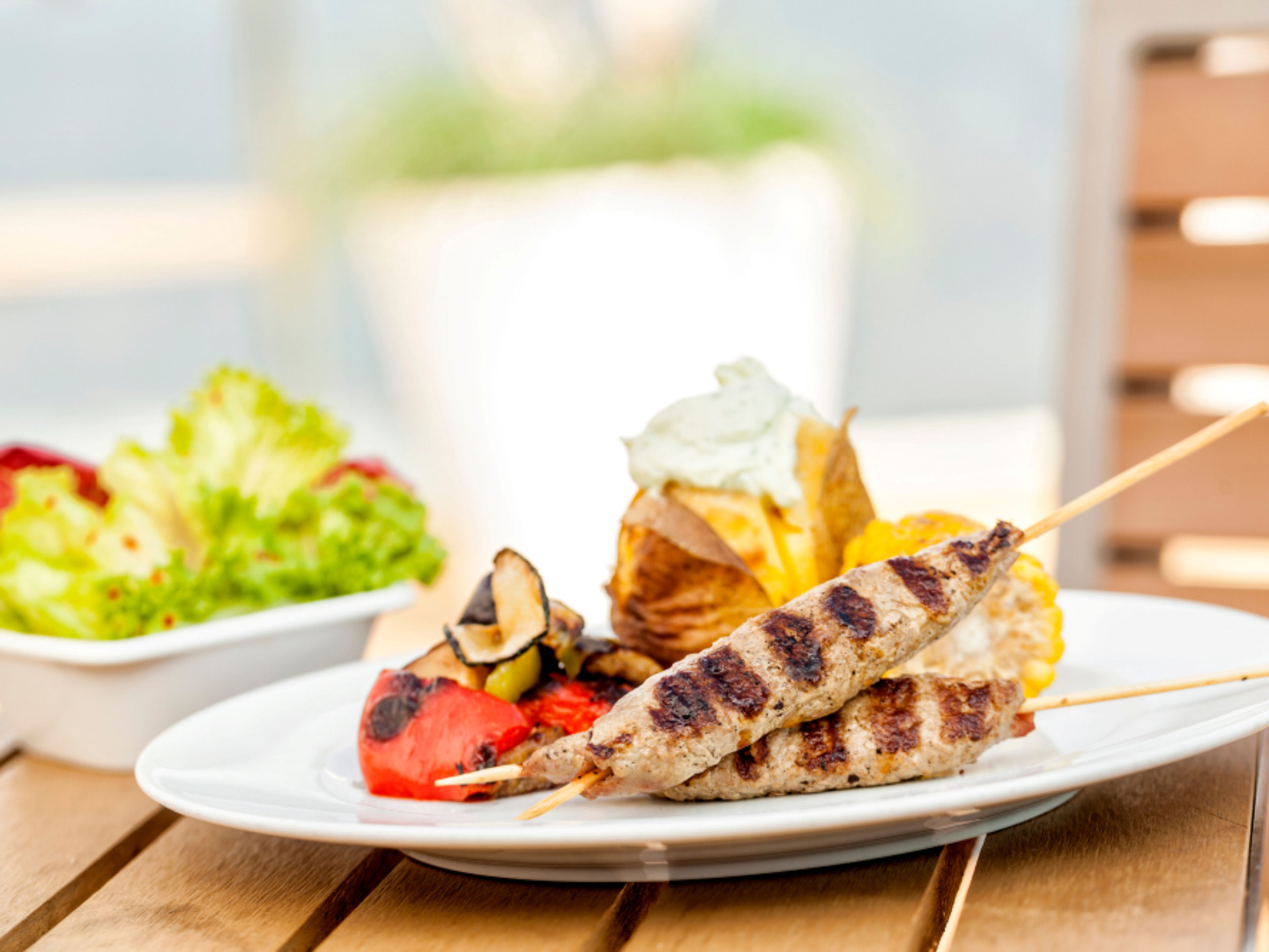 Grilled meat skewers with vegetables, a baked potato and a salad on a white plate. Grilled meat skewers with vegetables, a baked potato and a salad on a white plate.