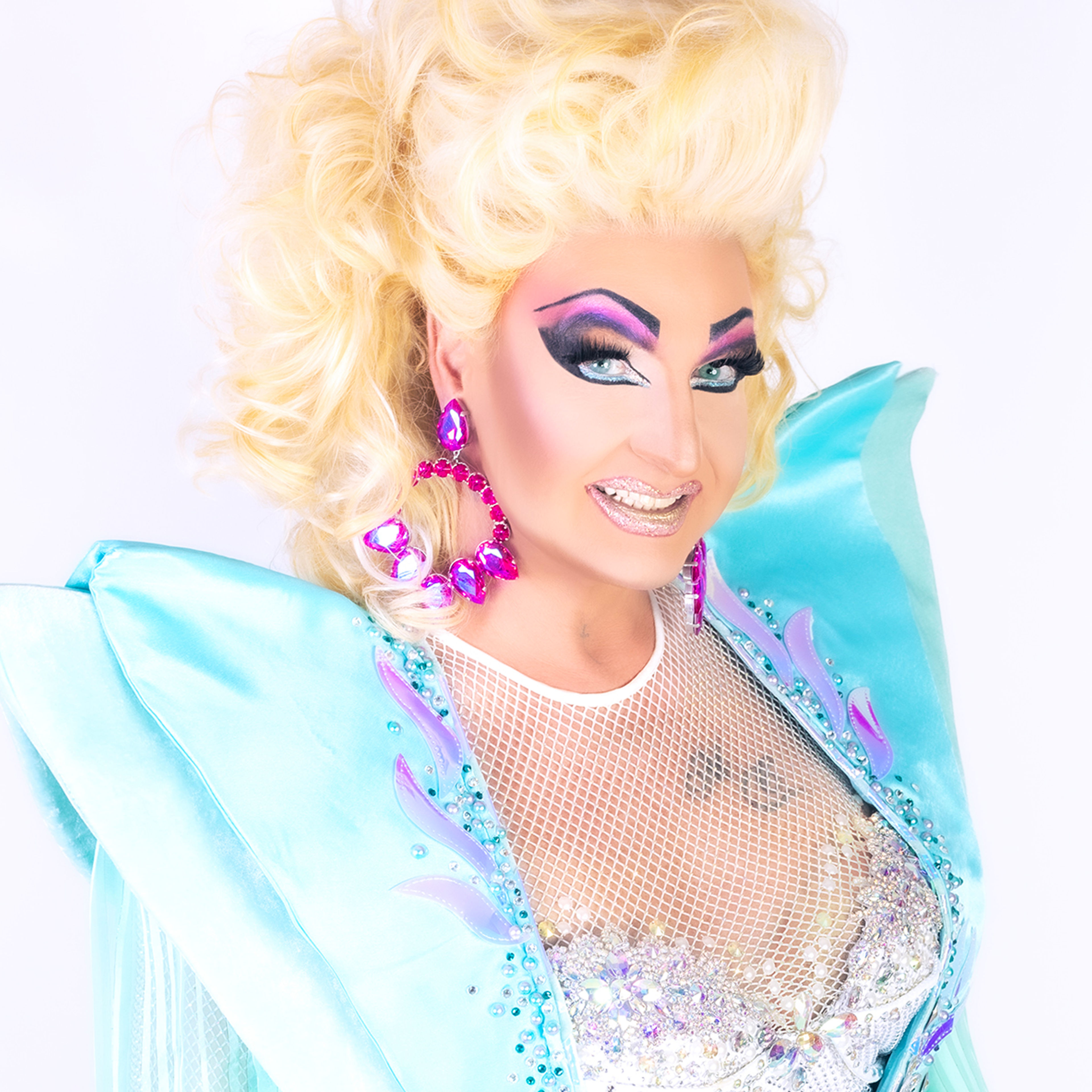 Drag Queen in türkisem Kostüm, blonder Perücke und pinken Ohrringen lächelt glamourös. Drag Queen in türkisem Kostüm, blonder Perücke und pinken Ohrringen lächelt glamourös.