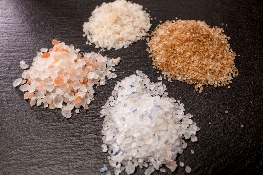 Four types of salt on a black background: pink, white, brown, blue.