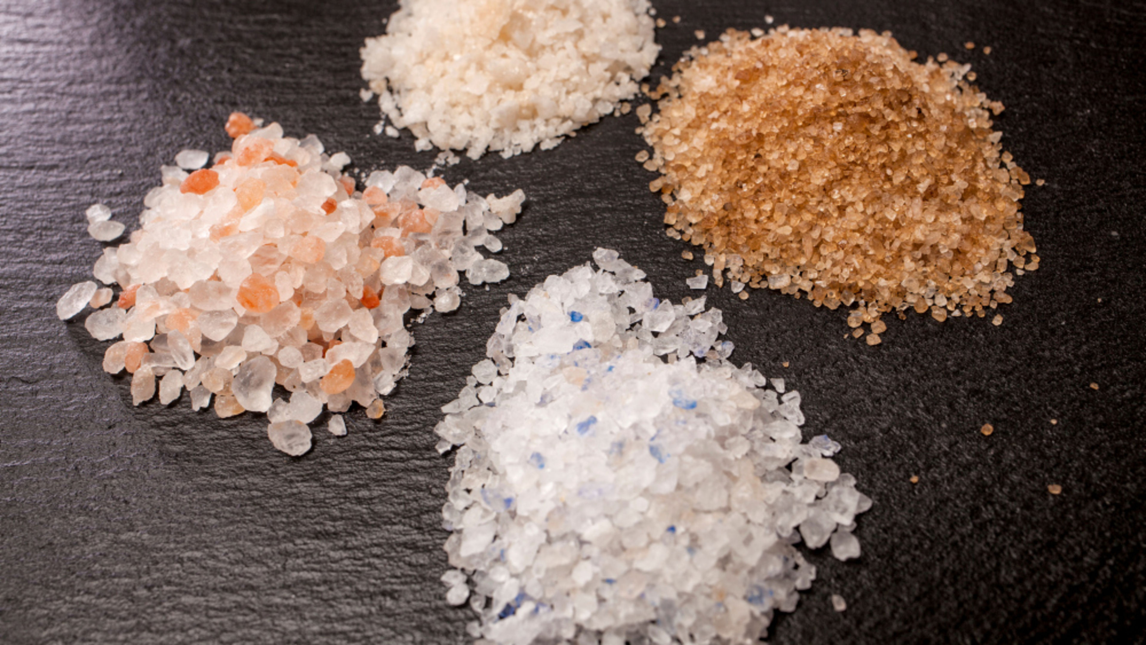 Four types of salt on a black background: pink, white, brown, blue. Four types of salt on a black background: pink, white, brown, blue.