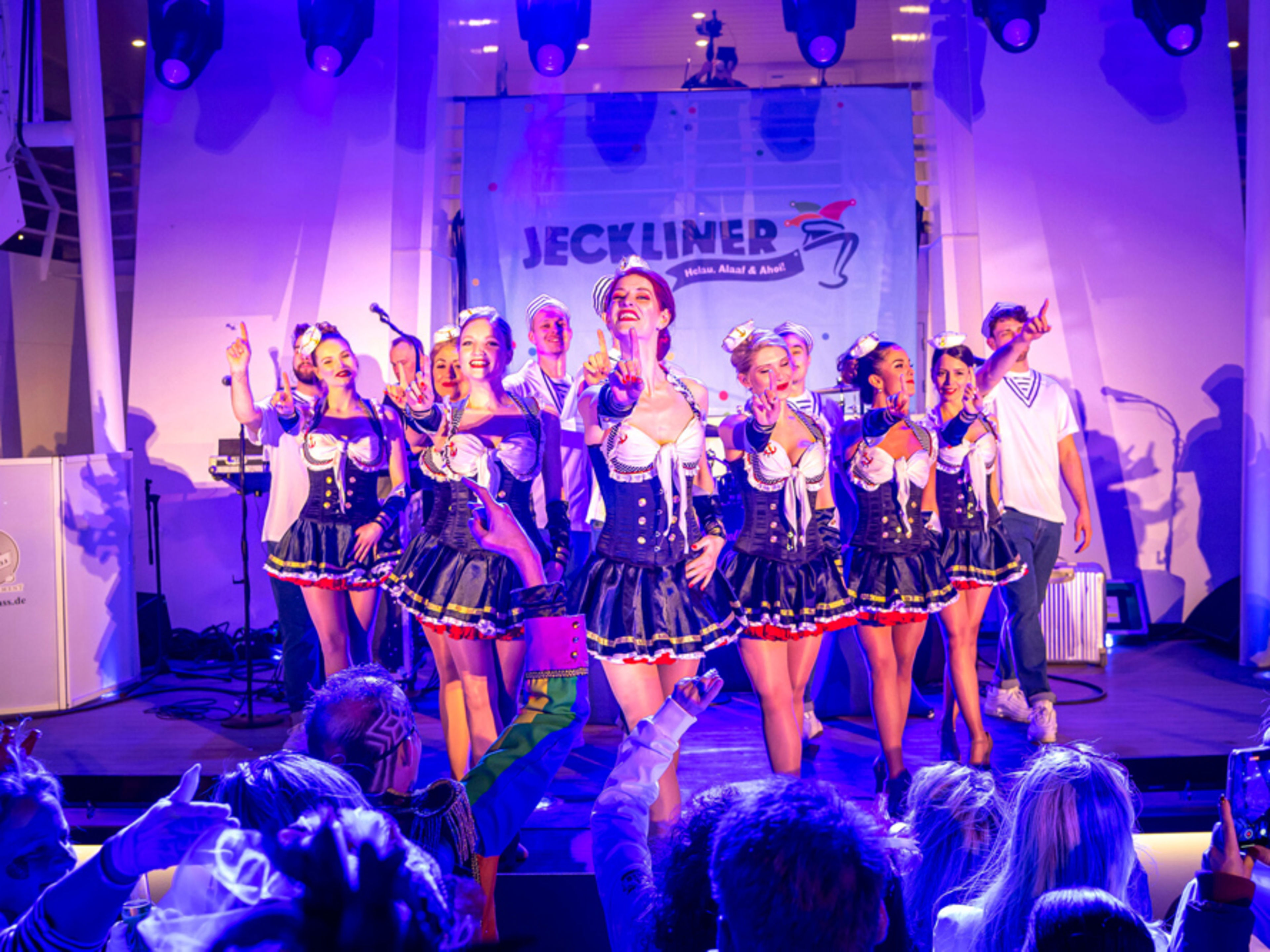 Jeckliner-Show: Tänzerinnen in Kostümen auf Bühne, blaues Licht, jubelndes Publikum Jeckliner-Show: Tänzerinnen in Kostümen auf Bühne, blaues Licht, jubelndes Publikum