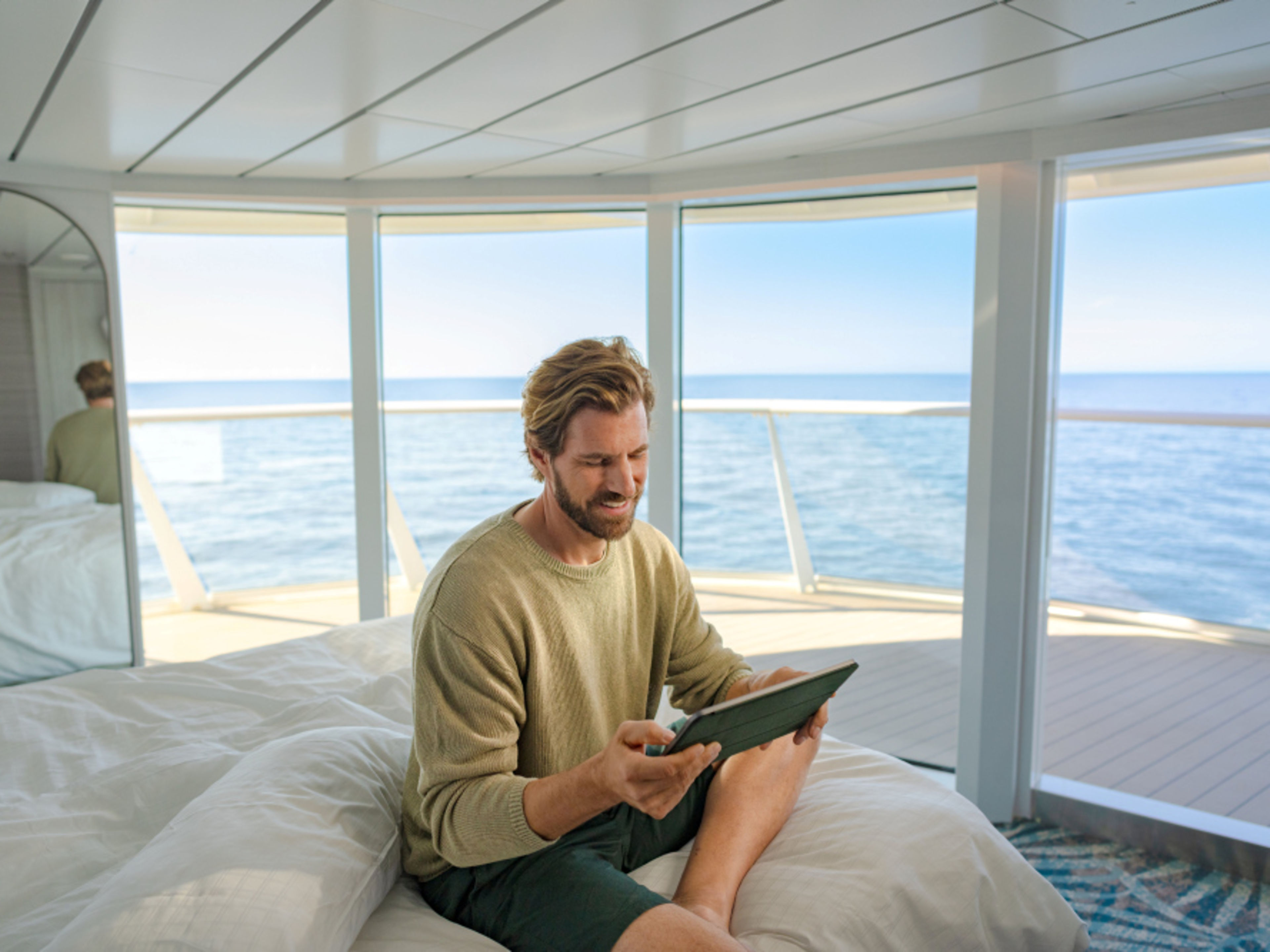 Mann sitzt mit Tablet auf Bett Mann sitzt mit Tablet auf Bett