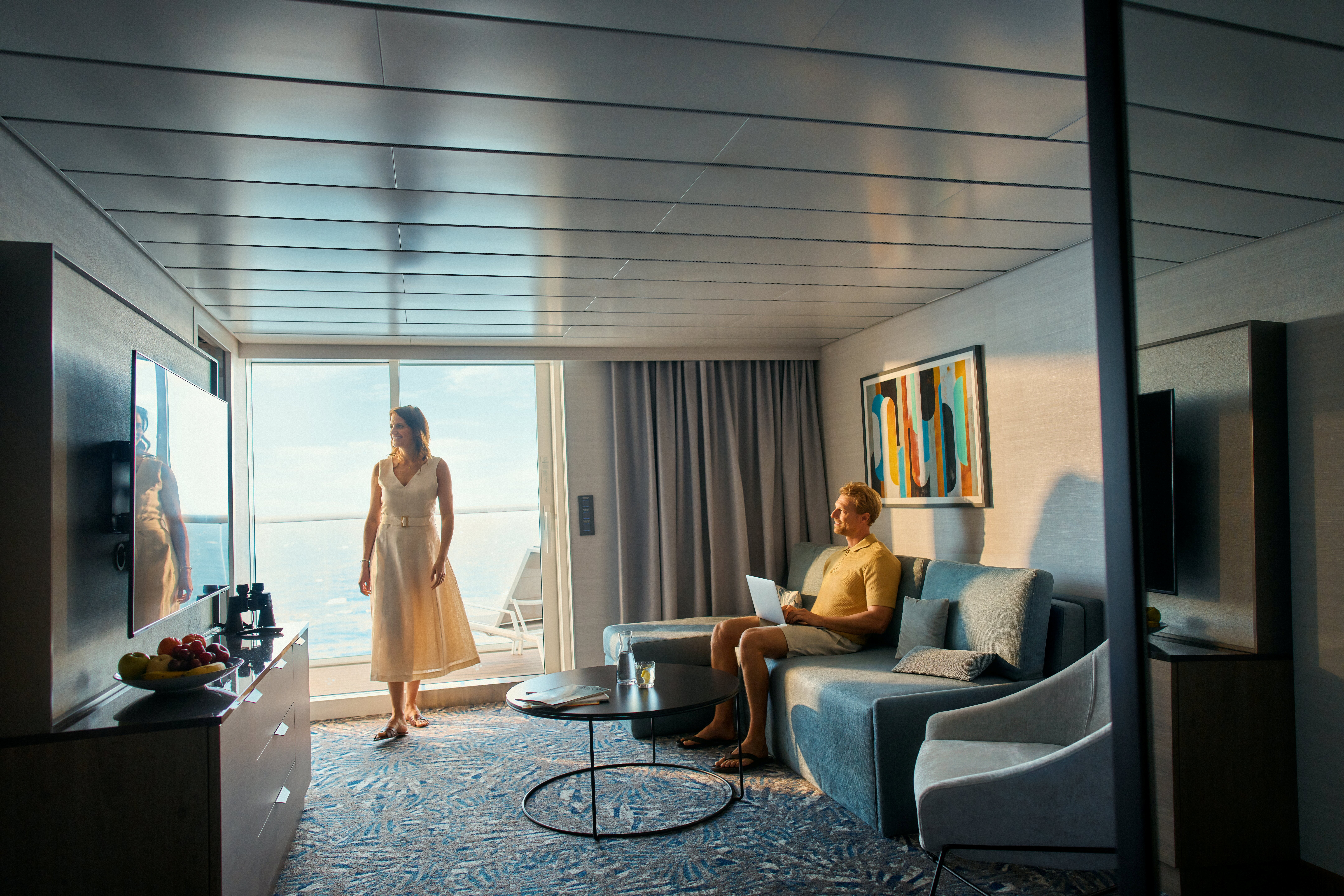 Paar entspannt in moderner Kreuzfahrt-Suite mit Meeresblick und Balkon.
