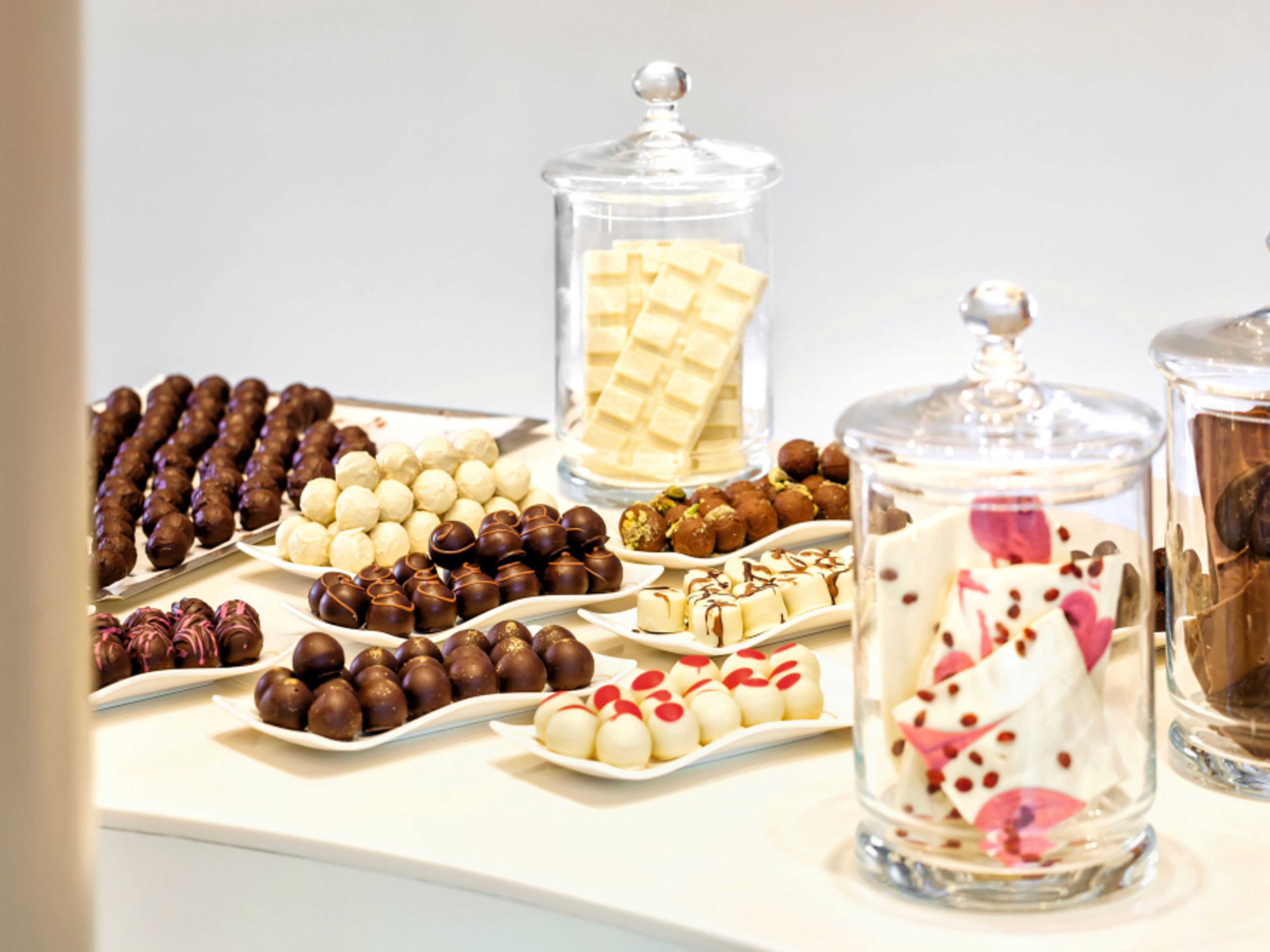 Elegante Pralinenteller und Glasgefäße mit weißer und dunkler Schokolade auf weißem Tisch. Elegante Pralinenteller und Glasgefäße mit weißer und dunkler Schokolade auf weißem Tisch.