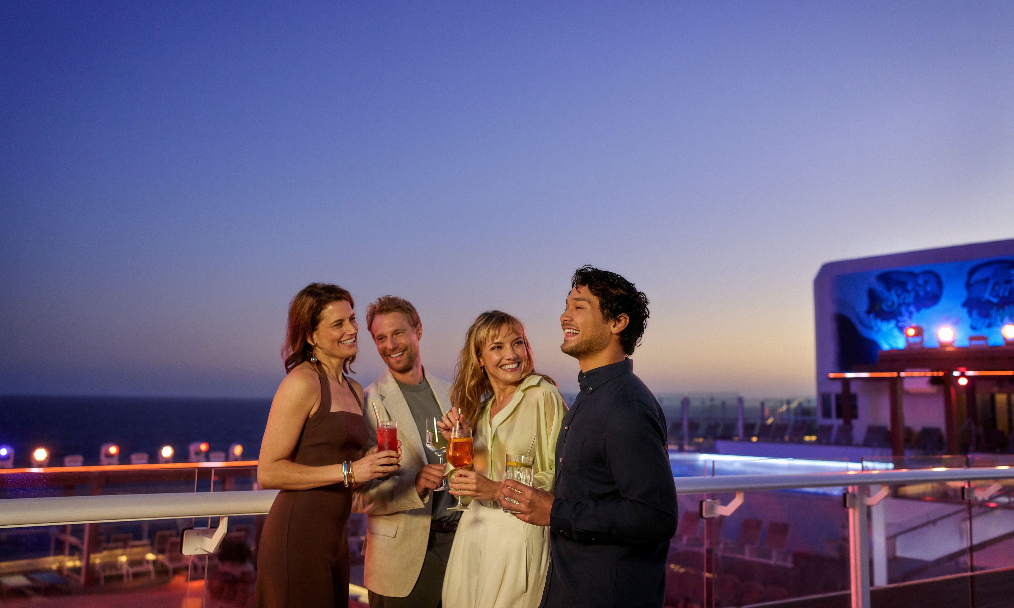 Vier fröhliche Menschen genießen Cocktails auf dem Deck eines Kreuzfahrtschiffs bei Abenddämmerung. Vier fröhliche Menschen genießen Cocktails auf dem Deck eines Kreuzfahrtschiffs bei Abenddämmerung.