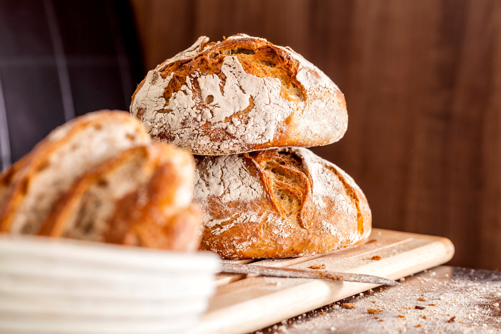 Two golden-brown loaves of artisan bread on a wooden board, dusted with flour.