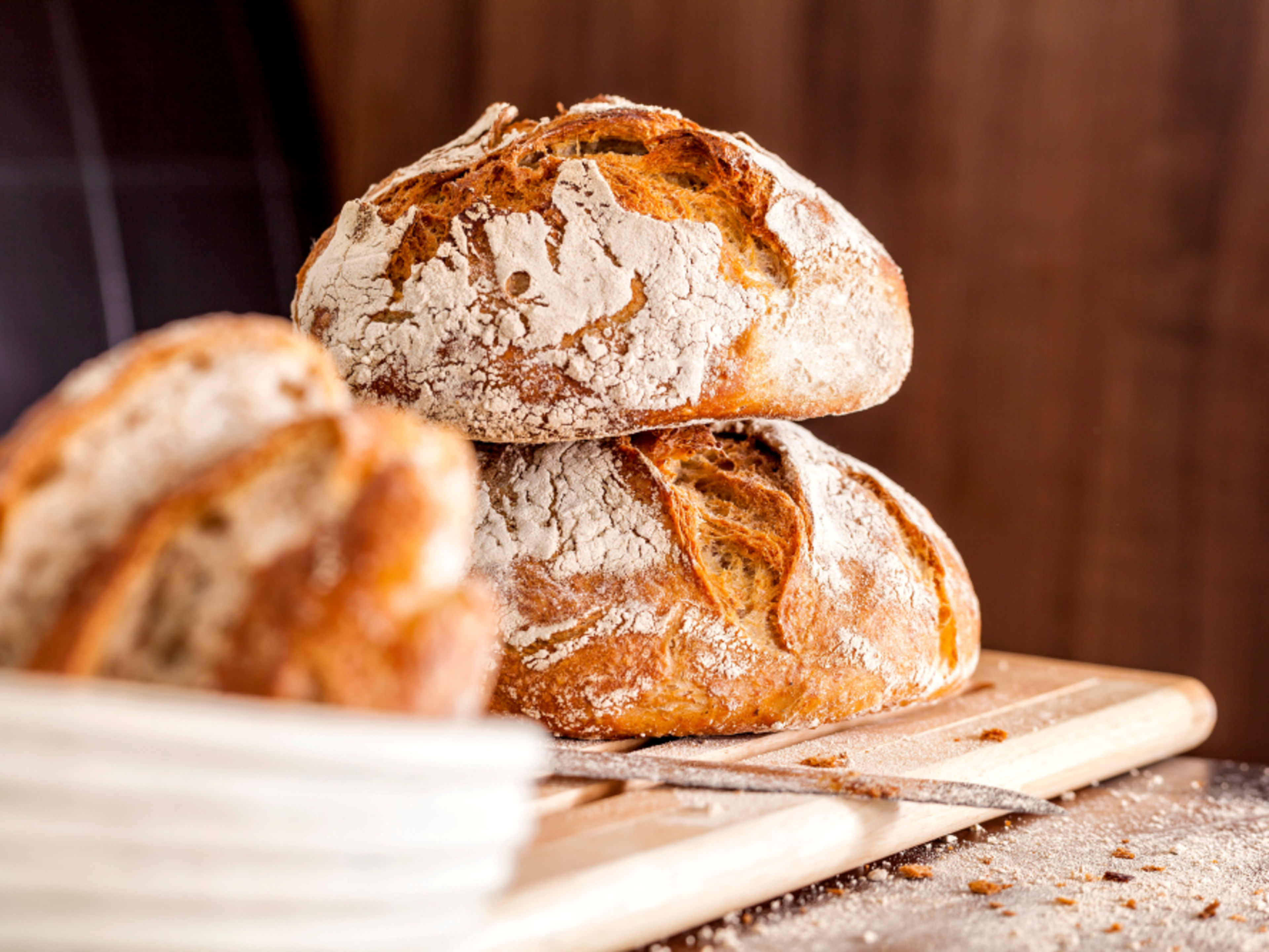 Two golden-brown loaves of artisan bread on a wooden board, dusted with flour. Two golden-brown loaves of artisan bread on a wooden board, dusted with flour.