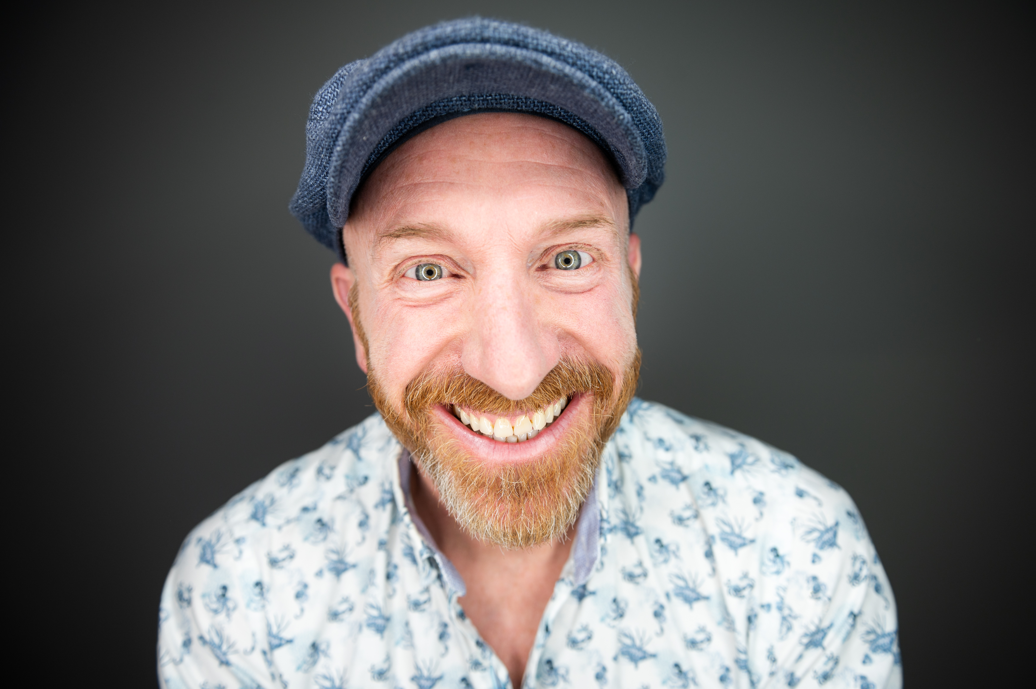 Mann mit rotem Bart und blauer Schiebermütze lacht breit in die Kamera.