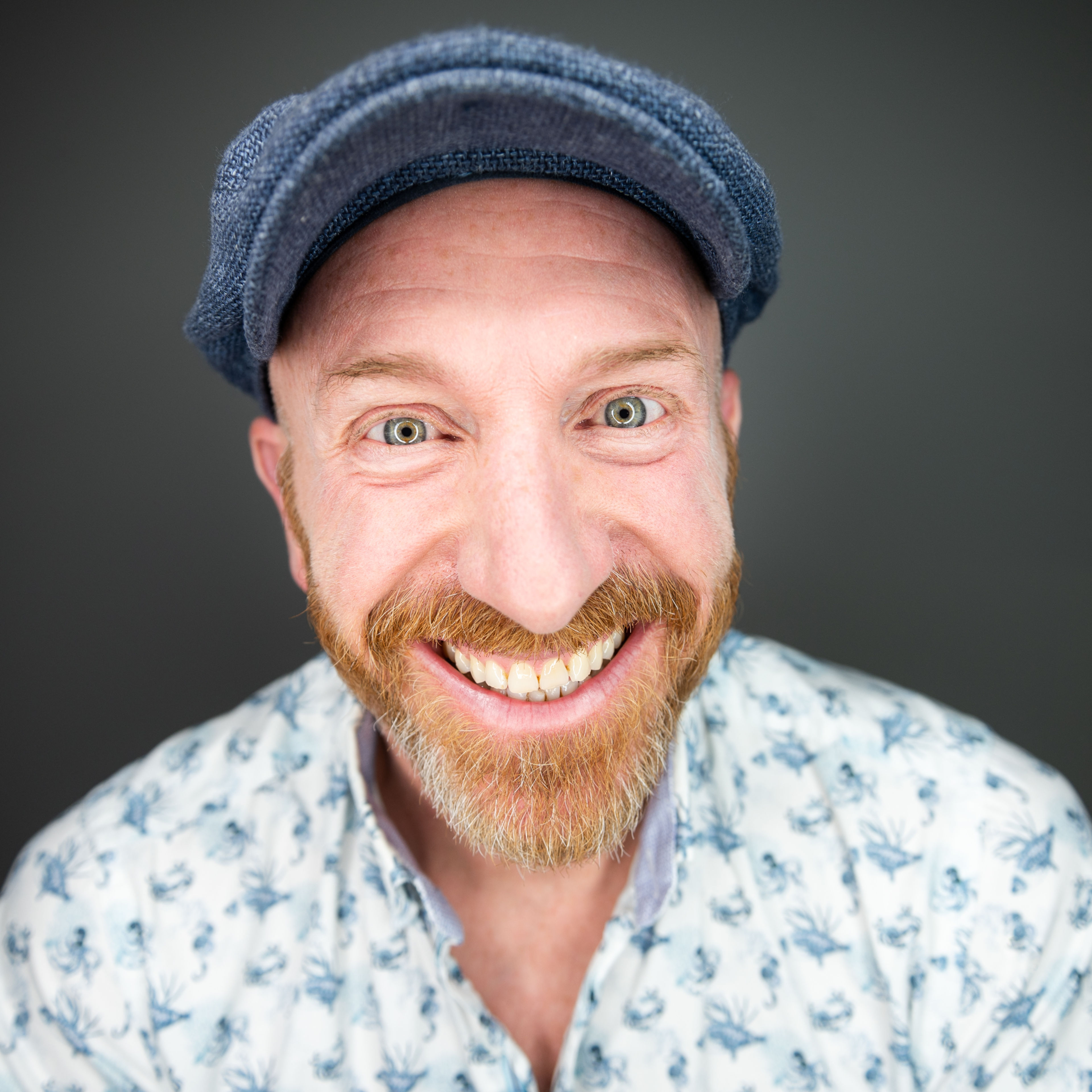 Mann mit rotem Bart und blauer Schiebermütze lacht breit in die Kamera. Mann mit rotem Bart und blauer Schiebermütze lacht breit in die Kamera.