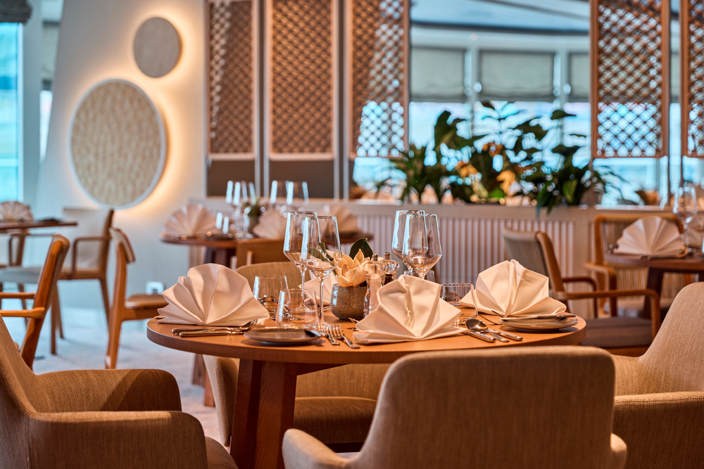 Elegant gedeckter Tisch in hellem Restaurant X-Coast mit Weingläsern und weißen Stoffservietten.