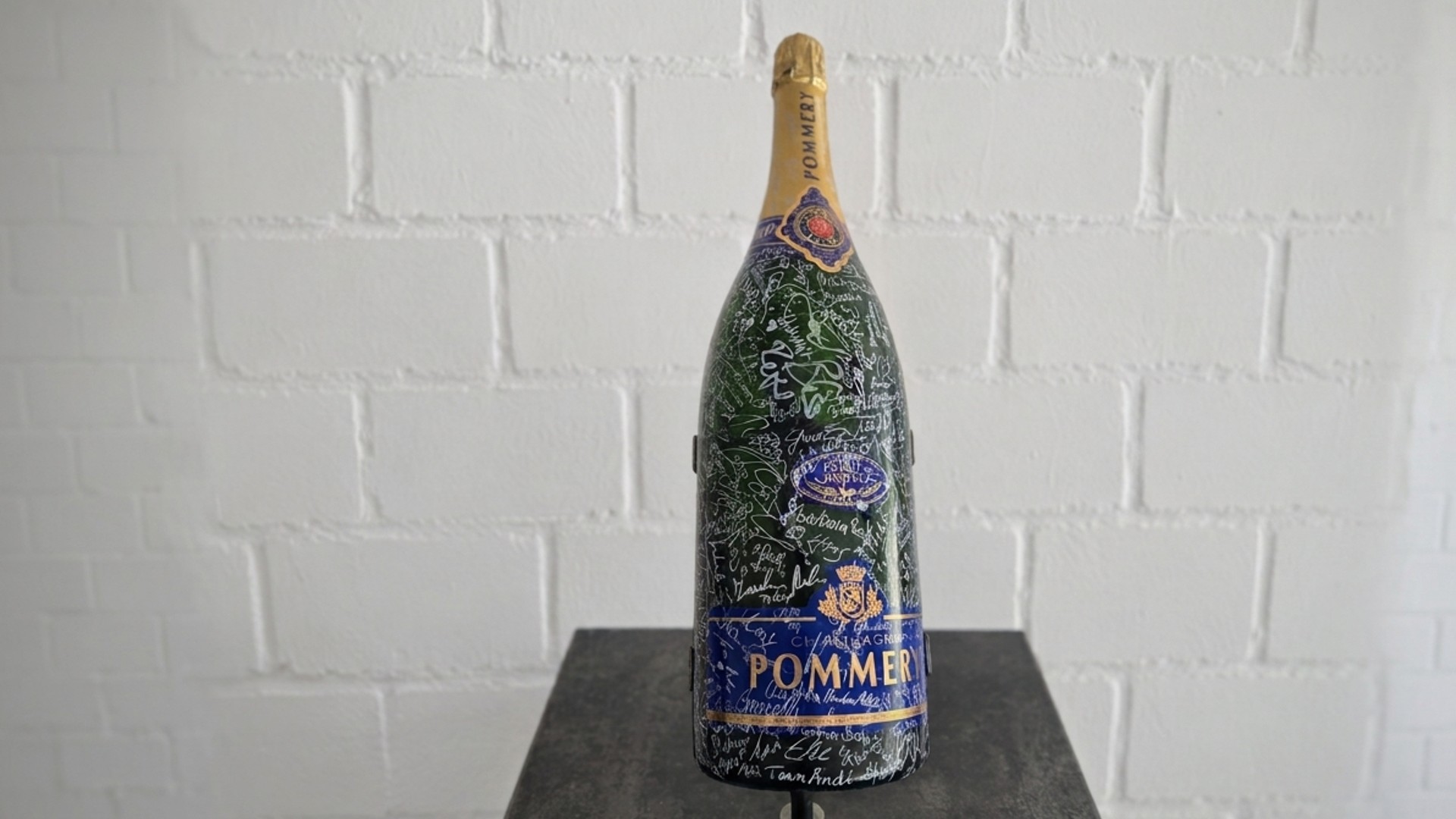 Große grüne Pommery Champagnerflasche mit vielen Autogrammen auf einem Sockel.
