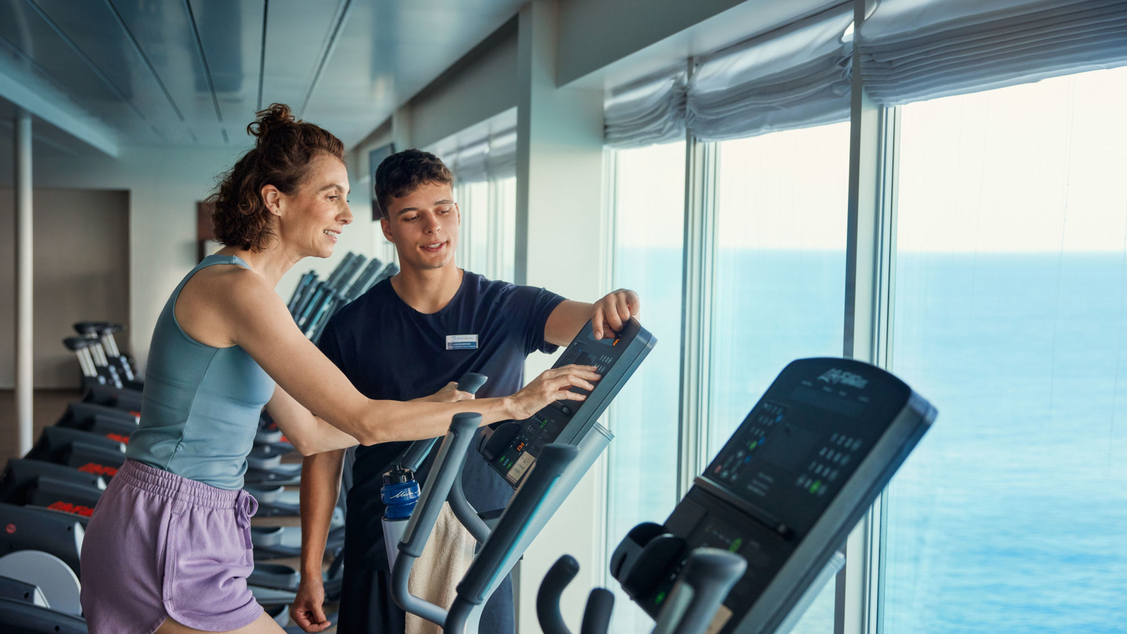Frau und Trainer im Fitnessstudio auf Kreuzfahrtschiff mit Meerblick. Frau und Trainer im Fitnessstudio auf Kreuzfahrtschiff mit Meerblick.