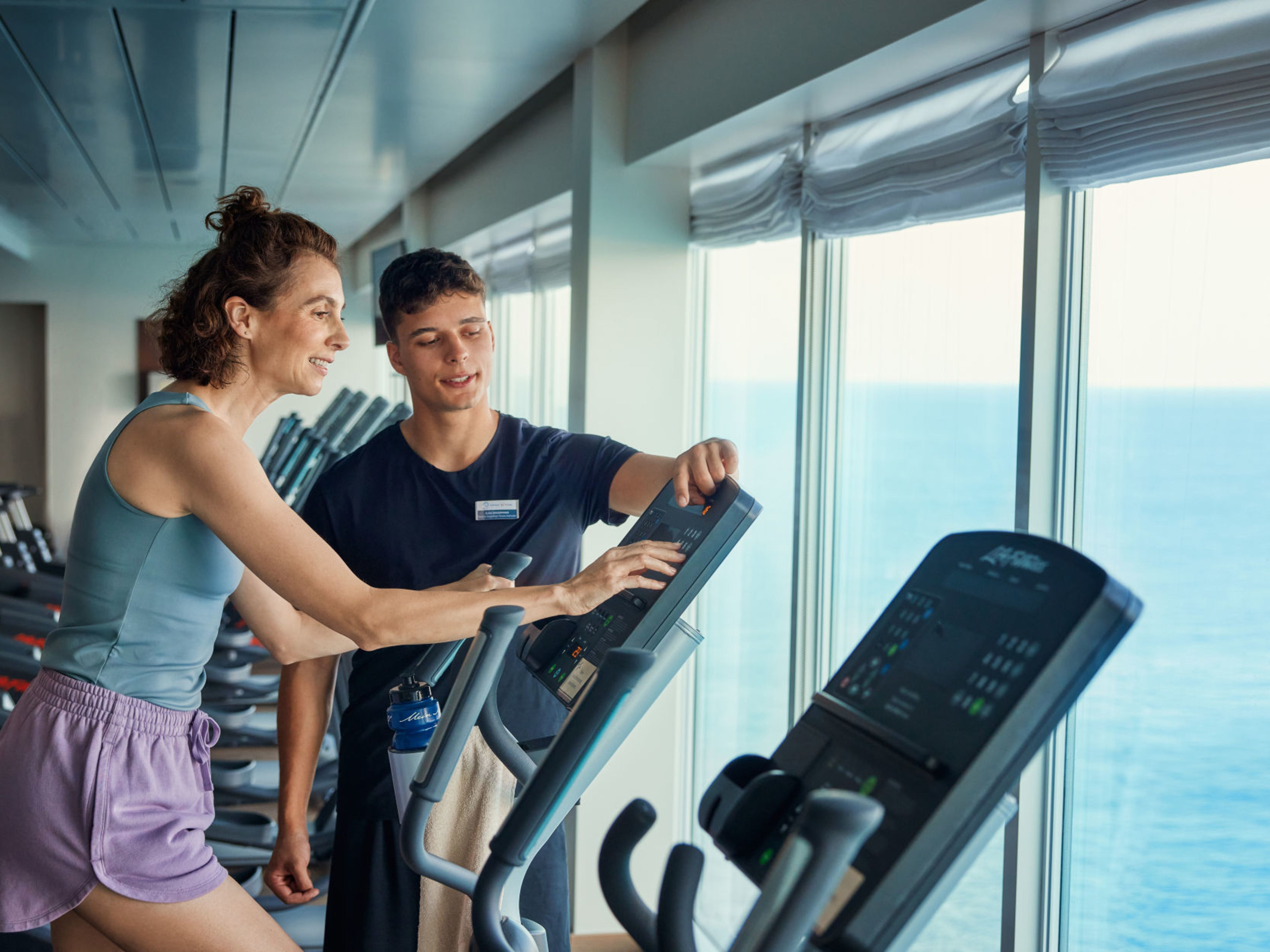 Frau und Trainer im Fitnessstudio auf Kreuzfahrtschiff mit Meerblick. Frau und Trainer im Fitnessstudio auf Kreuzfahrtschiff mit Meerblick.