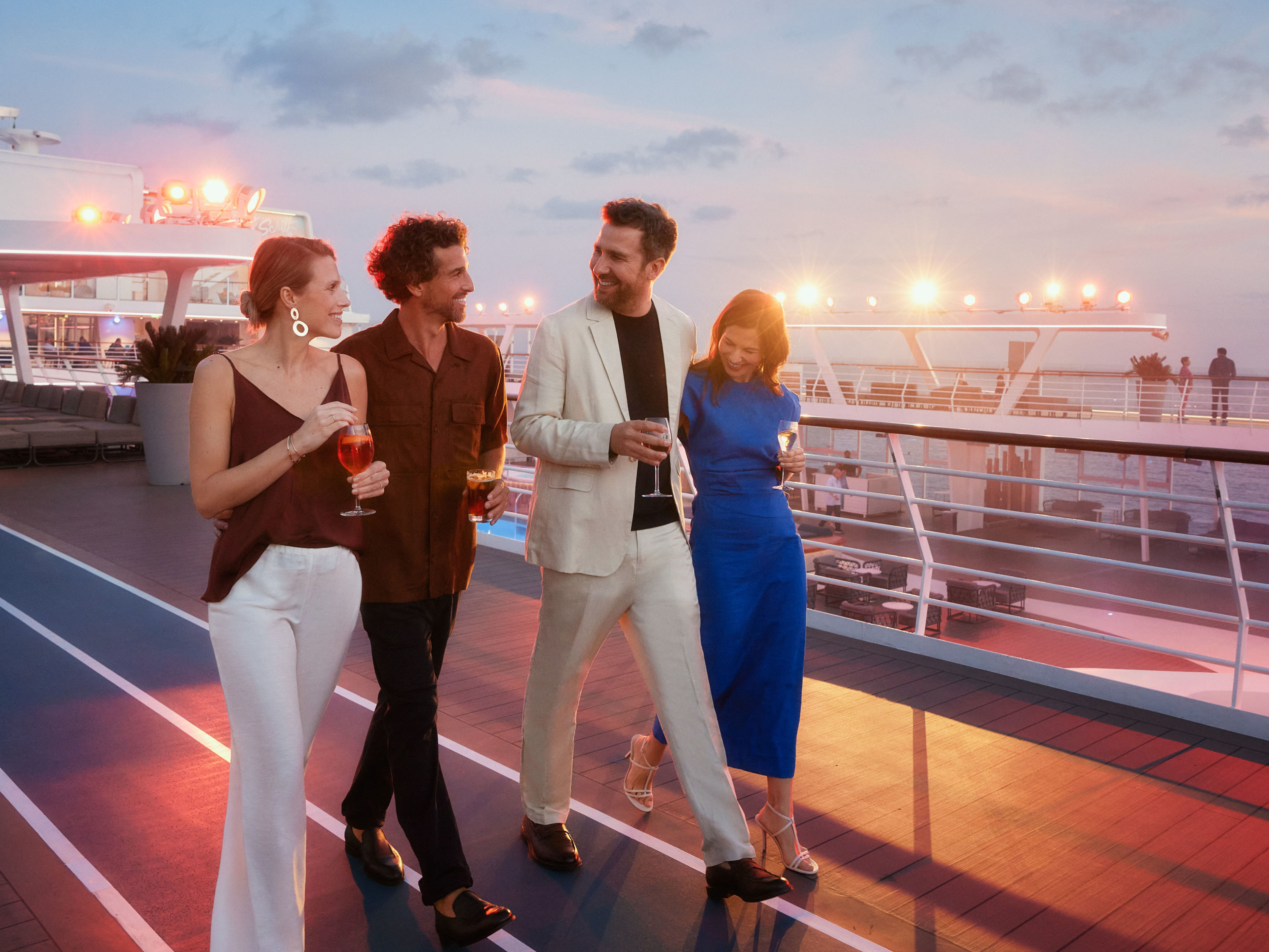 Vier Personen spazieren bei Sonnenuntergang auf einem Kreuzfahrtschiff der Mein Schiff® Flotte. Vier Personen spazieren bei Sonnenuntergang auf einem Kreuzfahrtschiff der Mein Schiff® Flotte.