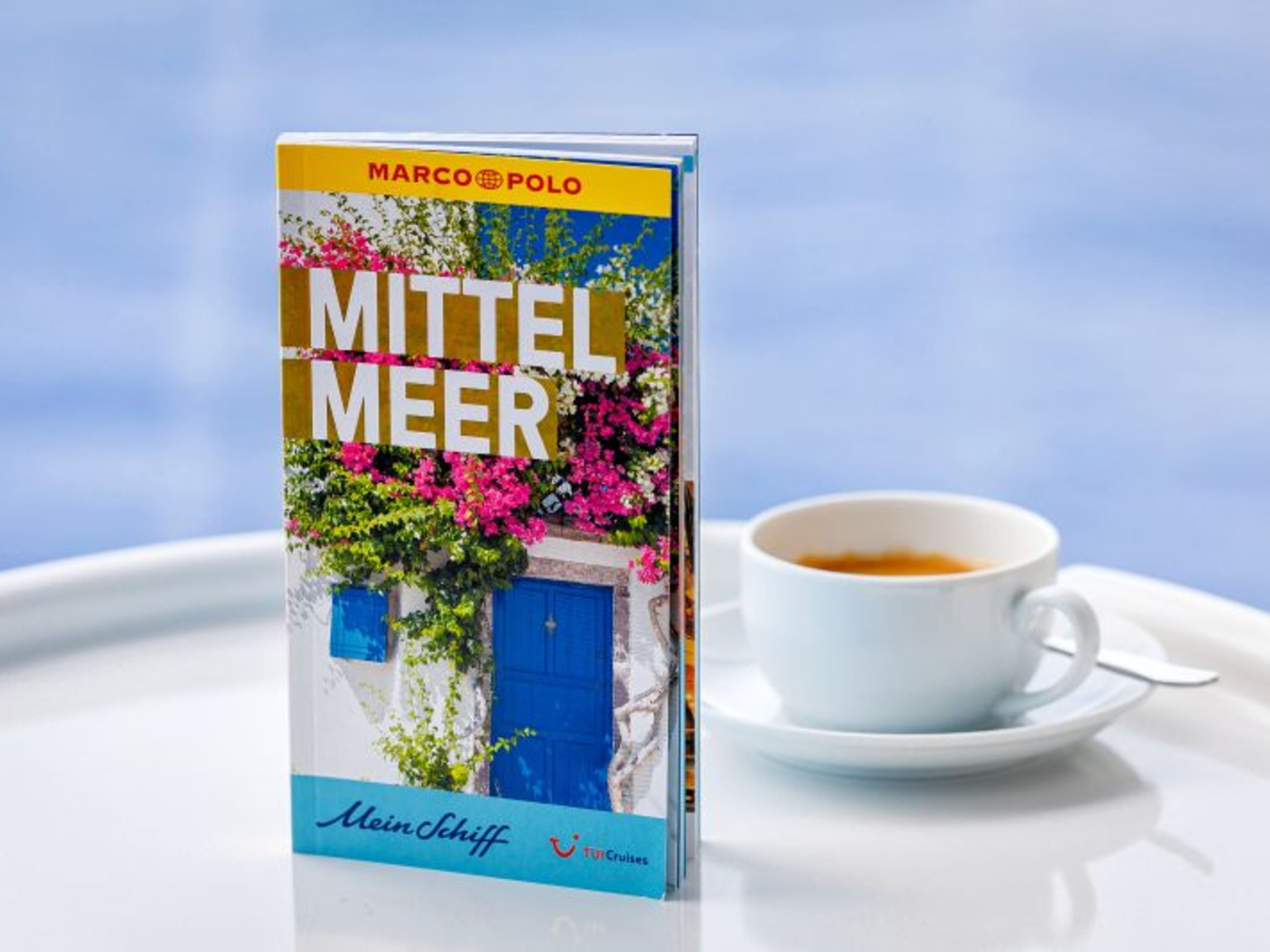 Reiseführer "Mittelmeer" neben einer Tasse Kaffee auf weißem Tisch. Reiseführer "Mittelmeer" neben einer Tasse Kaffee auf weißem Tisch.
