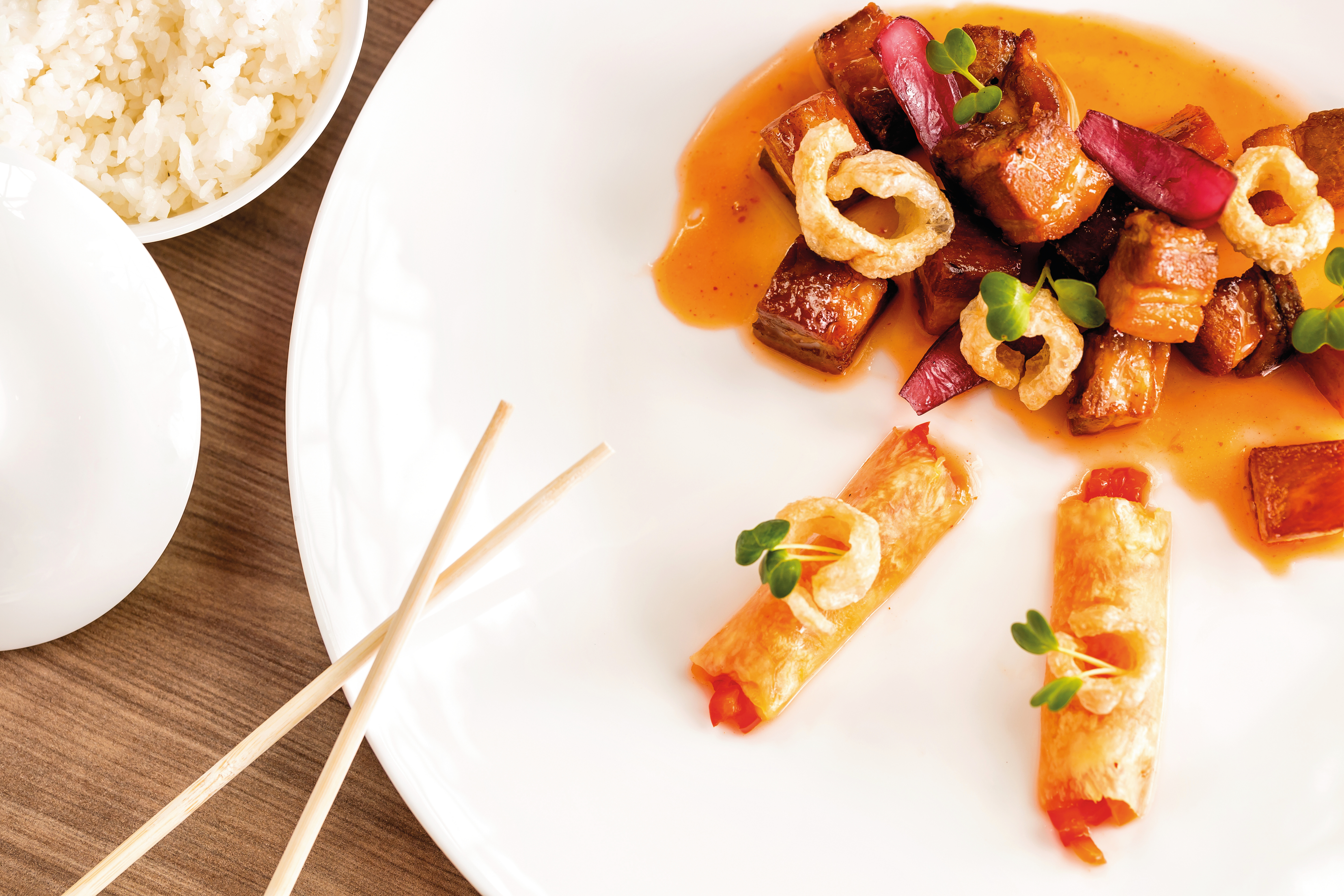 A gourmet dish featuring pork, vegetables, rice and chopsticks on a white plate.