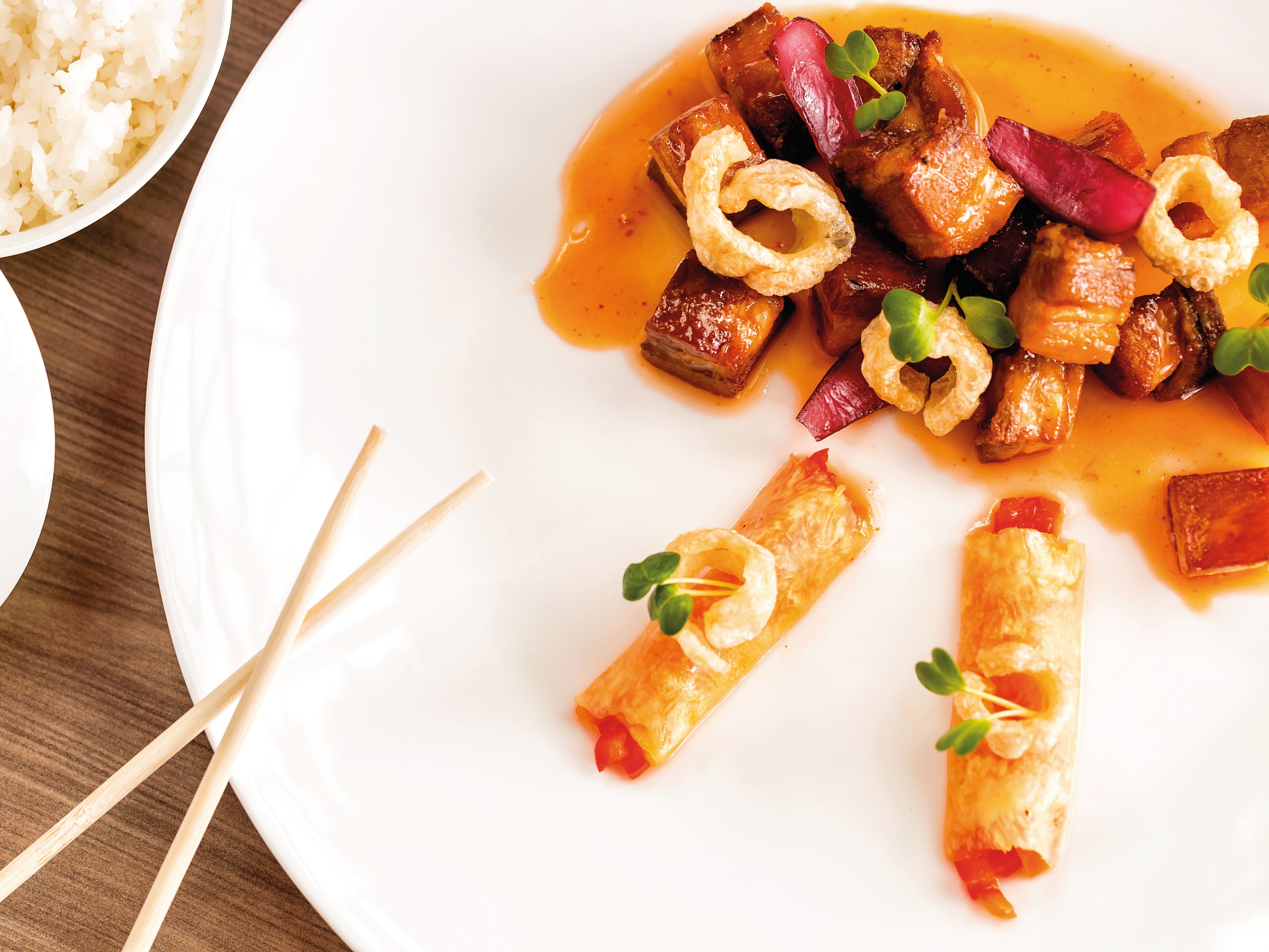 A gourmet dish featuring pork, vegetables, rice and chopsticks on a white plate. A gourmet dish featuring pork, vegetables, rice and chopsticks on a white plate.