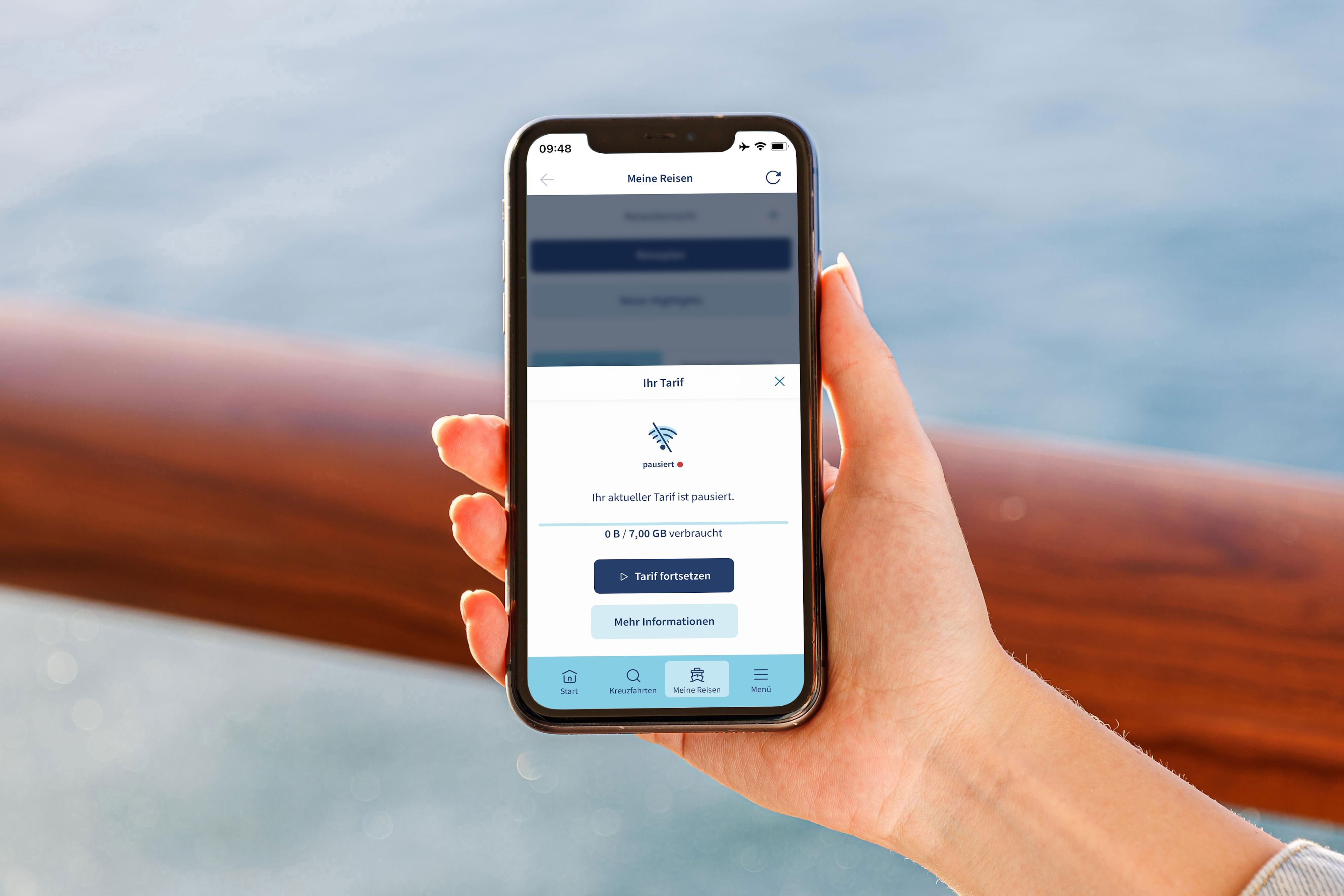 Hand hält Smartphone mit App, Meer im Hintergrund.