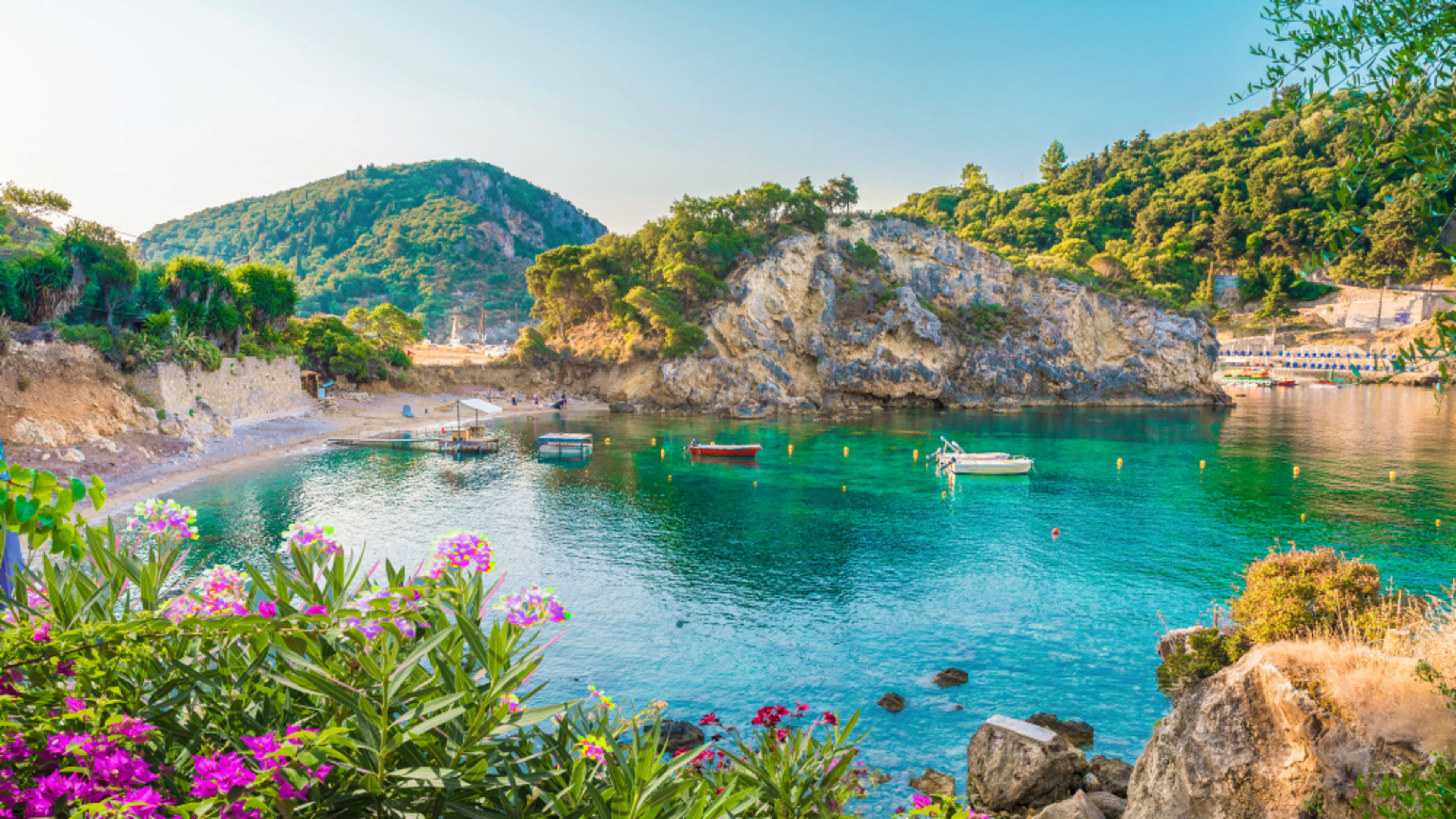 Bucht auf Korfu mit türkisfarbenem Wasser, Booten und Blumen. Bucht auf Korfu mit türkisfarbenem Wasser, Booten und Blumen.