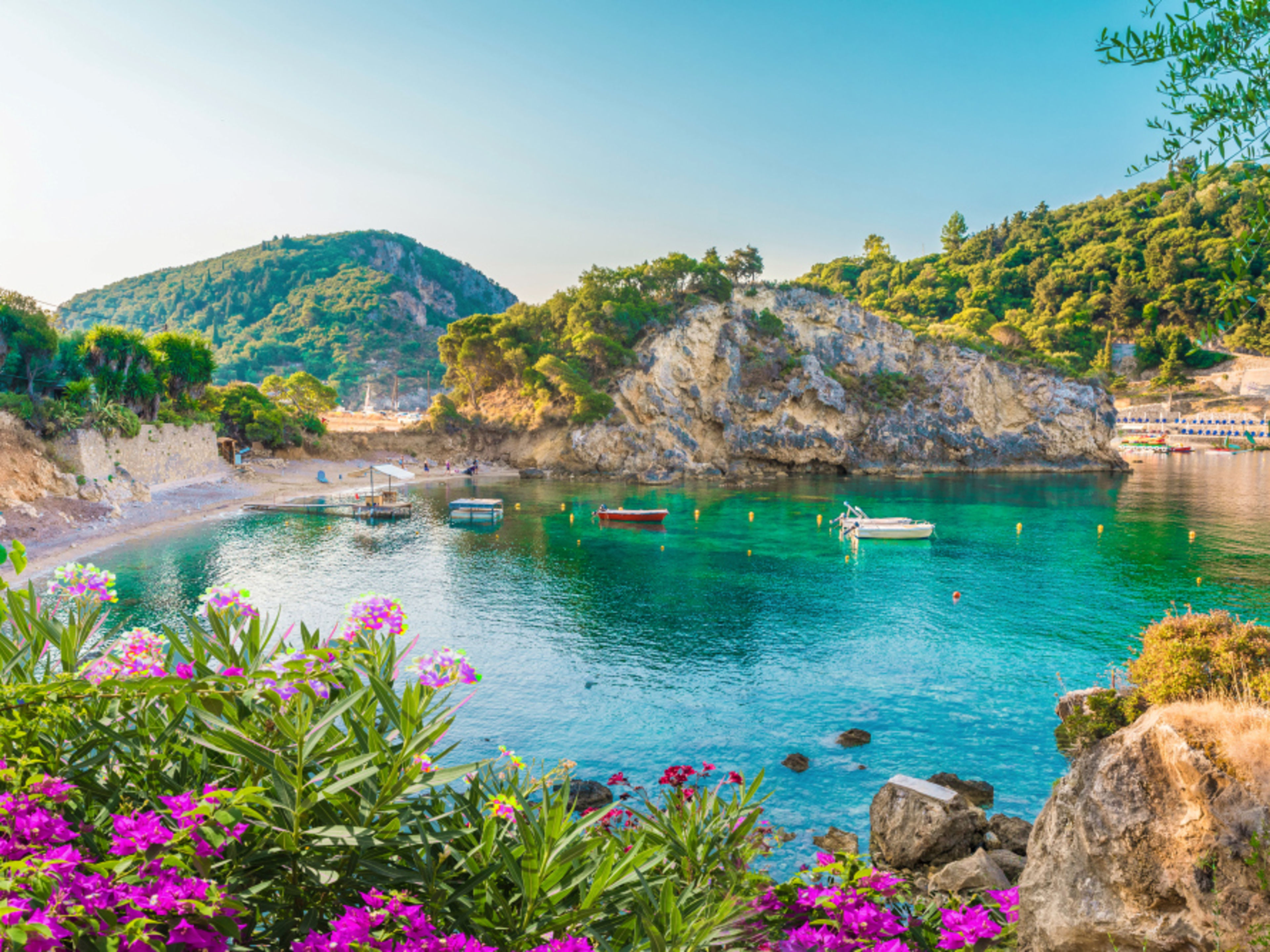 Bucht auf Korfu mit türkisfarbenem Wasser, Booten und Blumen. Bucht auf Korfu mit türkisfarbenem Wasser, Booten und Blumen.