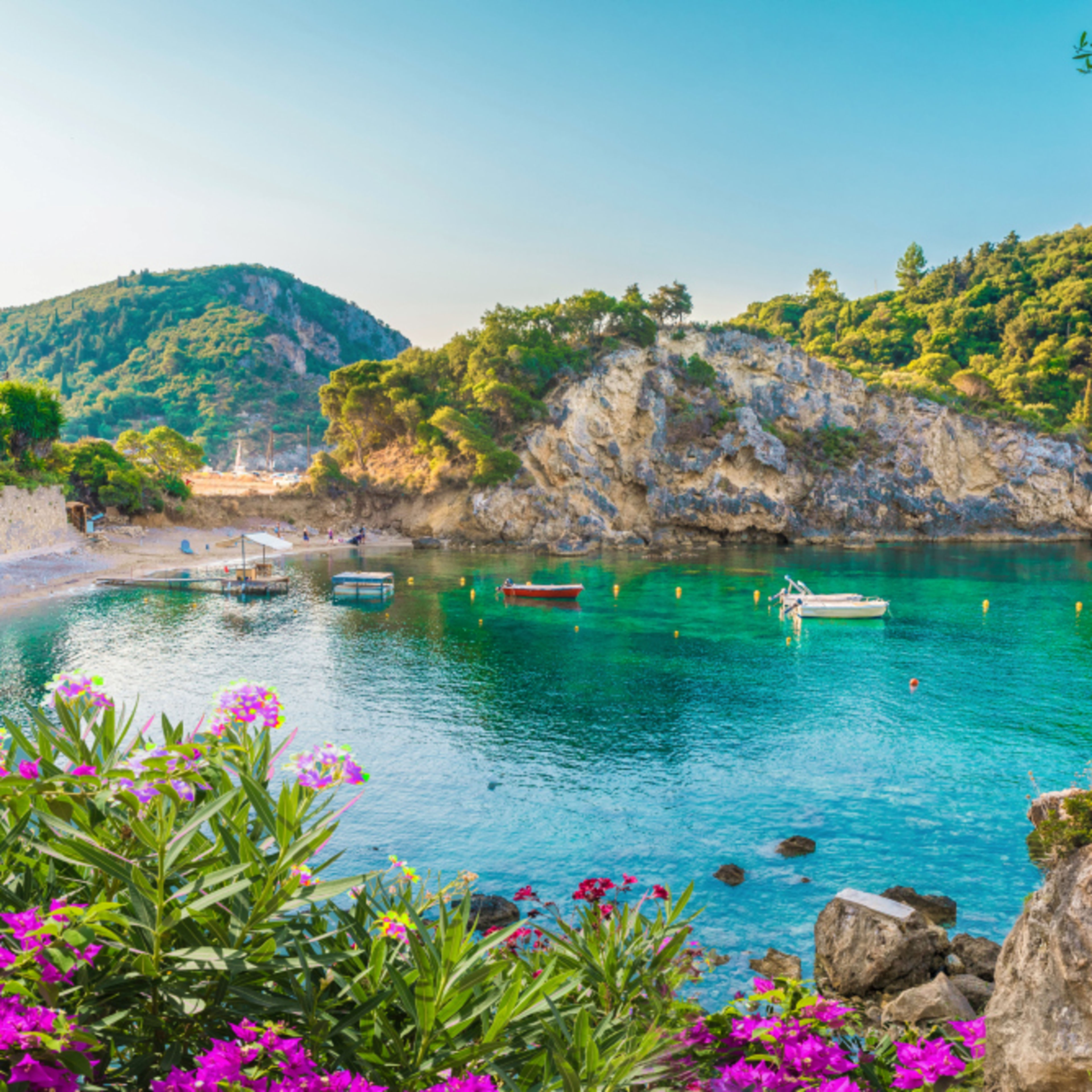 Bucht auf Korfu mit türkisfarbenem Wasser, Booten und Blumen. Bucht auf Korfu mit türkisfarbenem Wasser, Booten und Blumen.