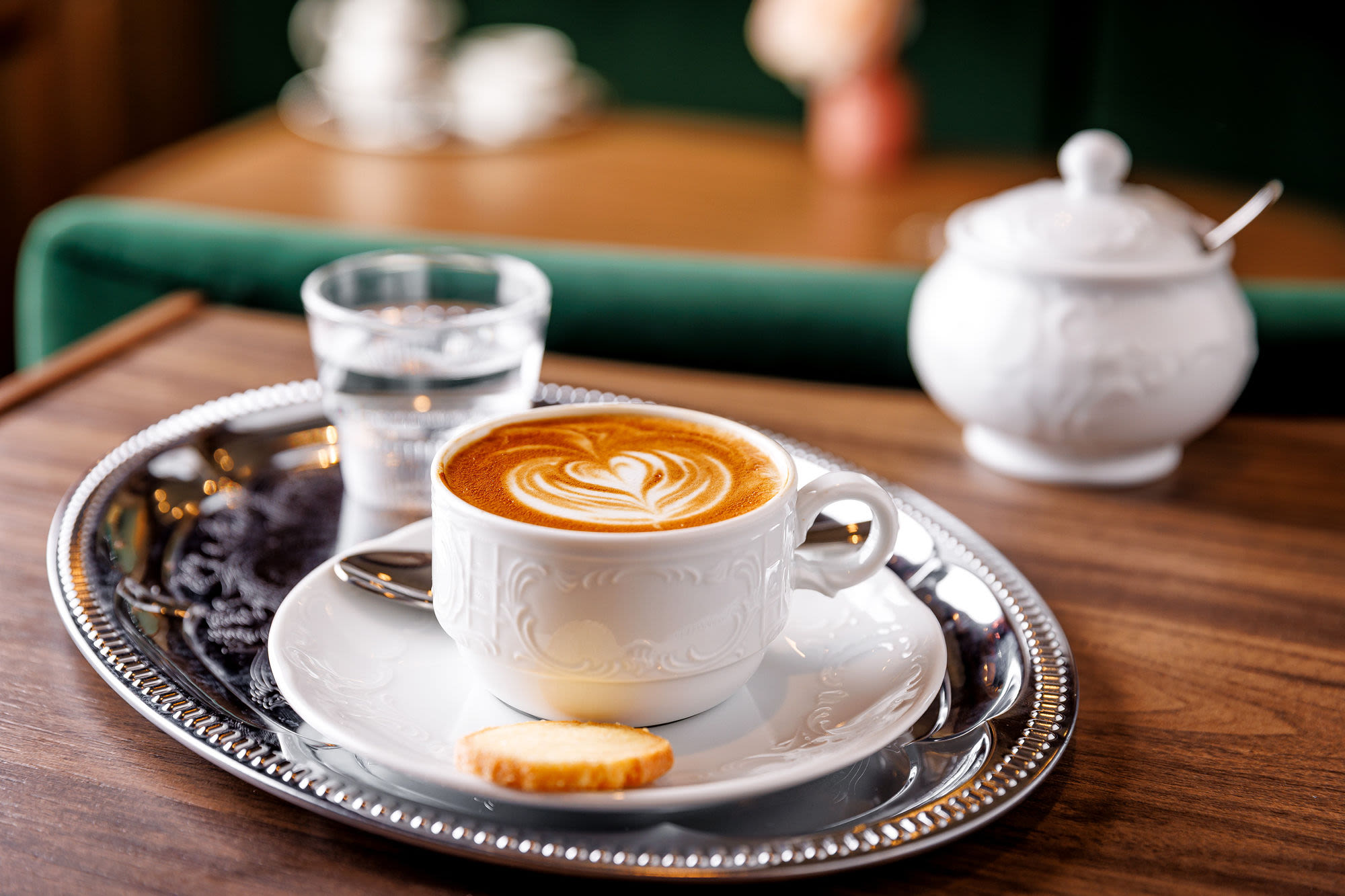 Kaffee mit Latte Art auf Tablett, Keks, Glas Wasser.