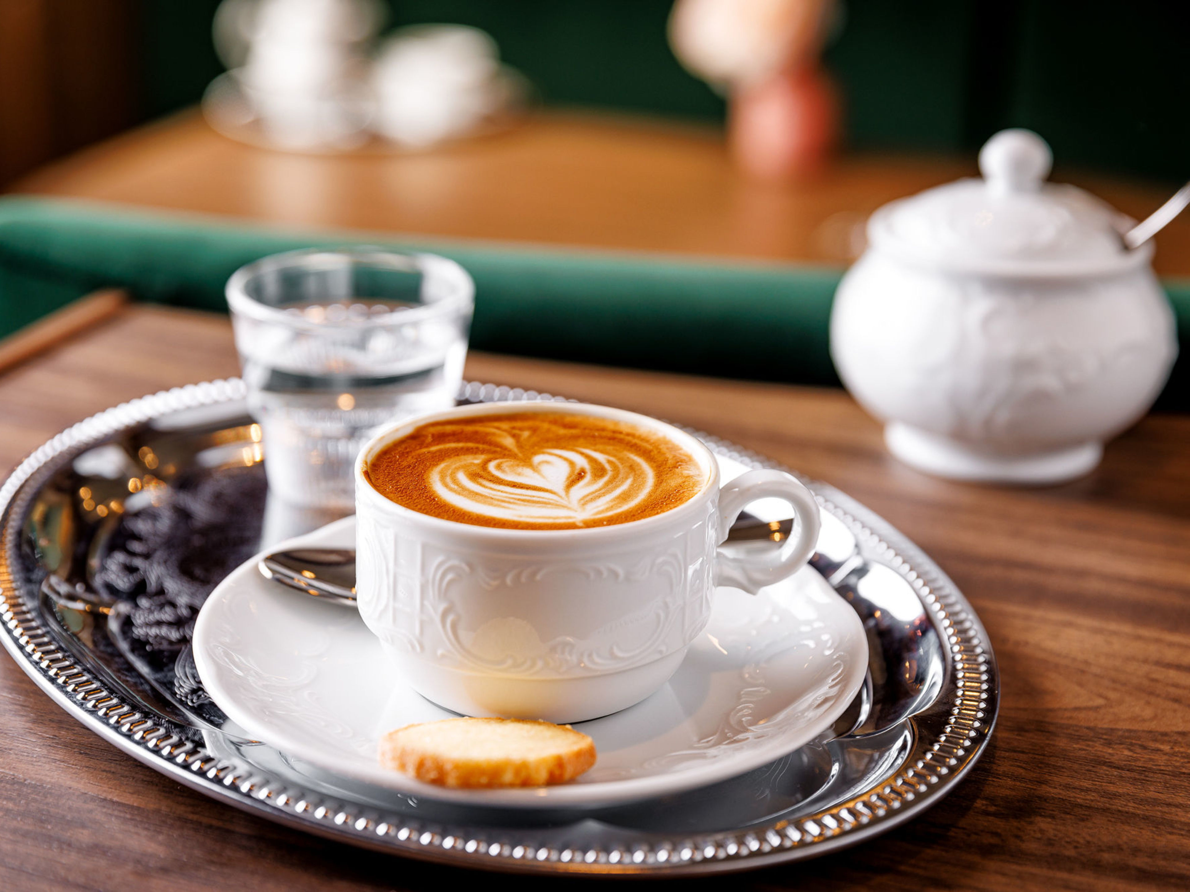Kaffee mit Latte Art auf Tablett, Keks, Glas Wasser. Kaffee mit Latte Art auf Tablett, Keks, Glas Wasser.