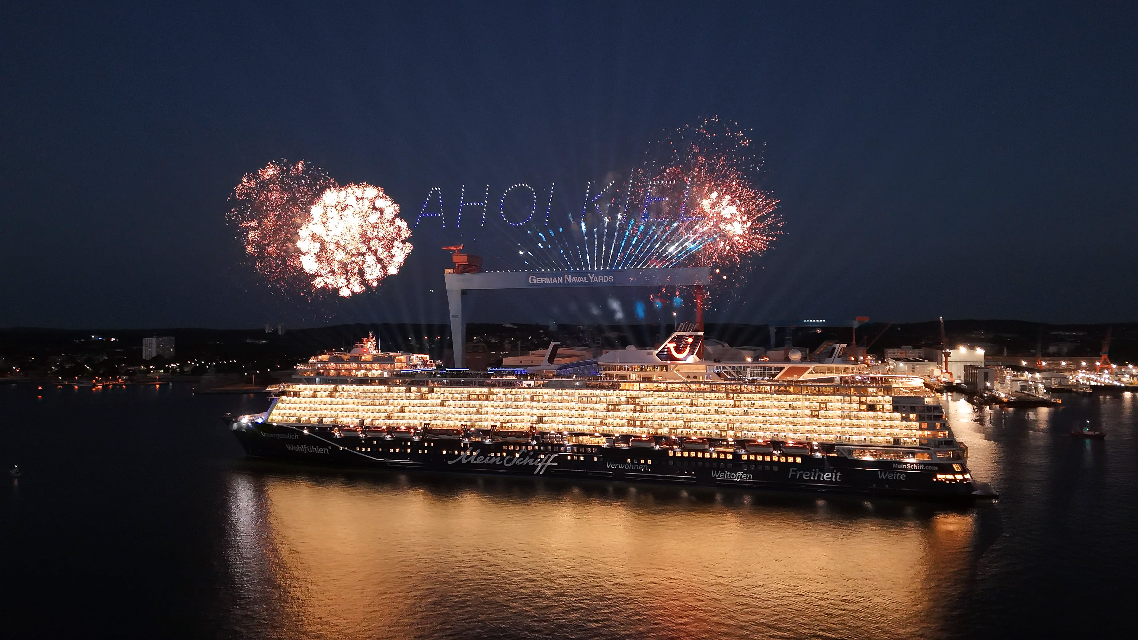 Kreuzfahrtschiff der Mein Schiff® Flotte bei Nacht mit Feuerwerk in Kiel.