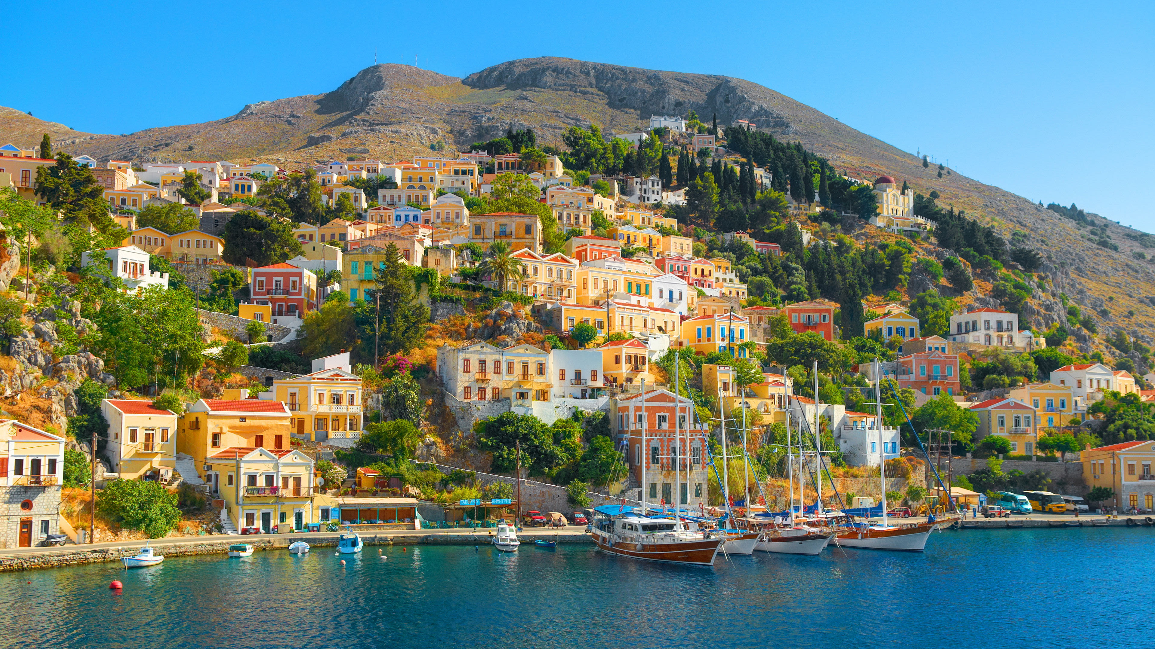 Bunte Häuser auf Symi, Griechenland, am Hang mit Segelbooten im Hafen.