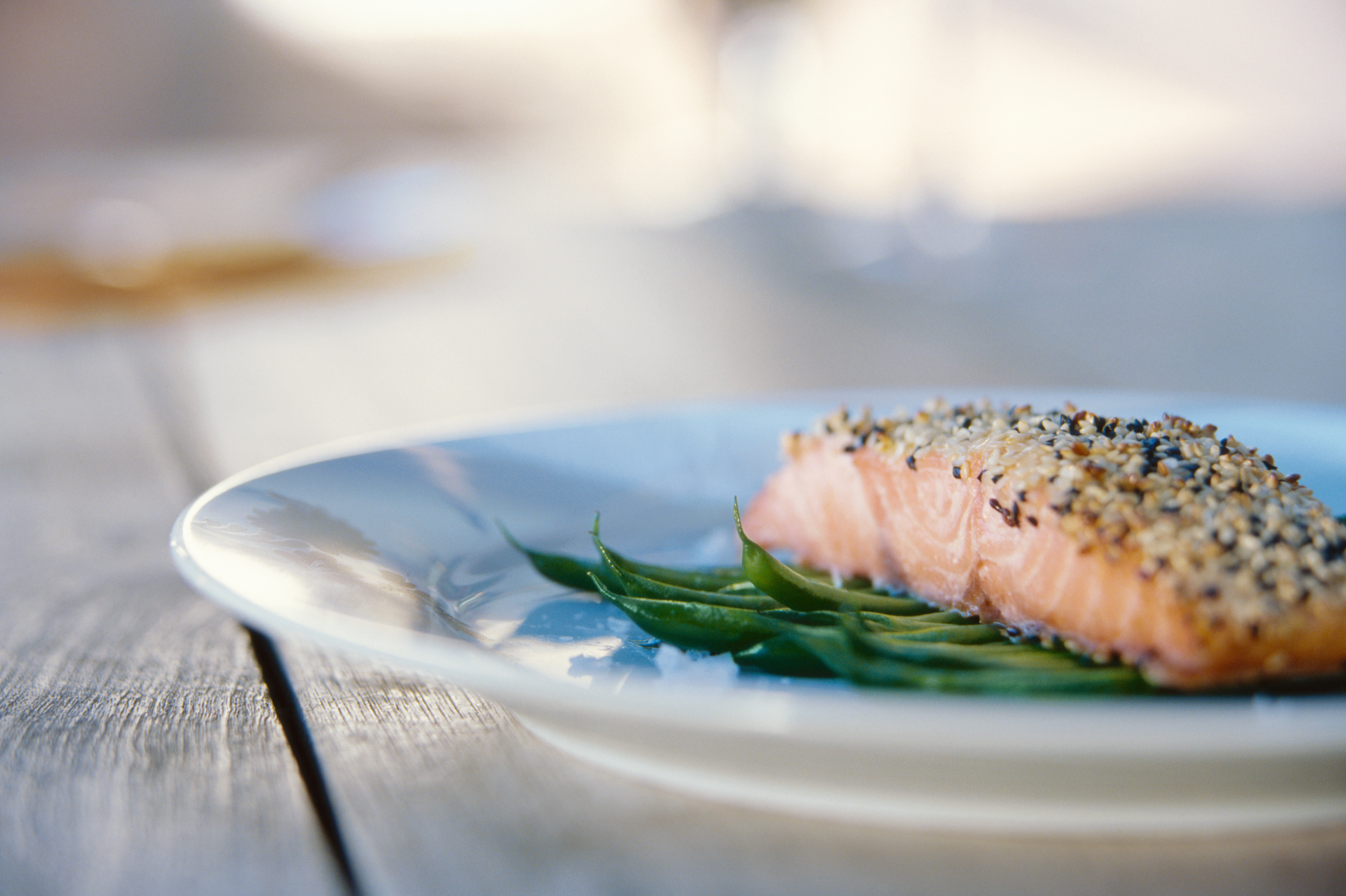 Salmon fillet with a sesame crust served on a bed of green vegetables on a white plate.
