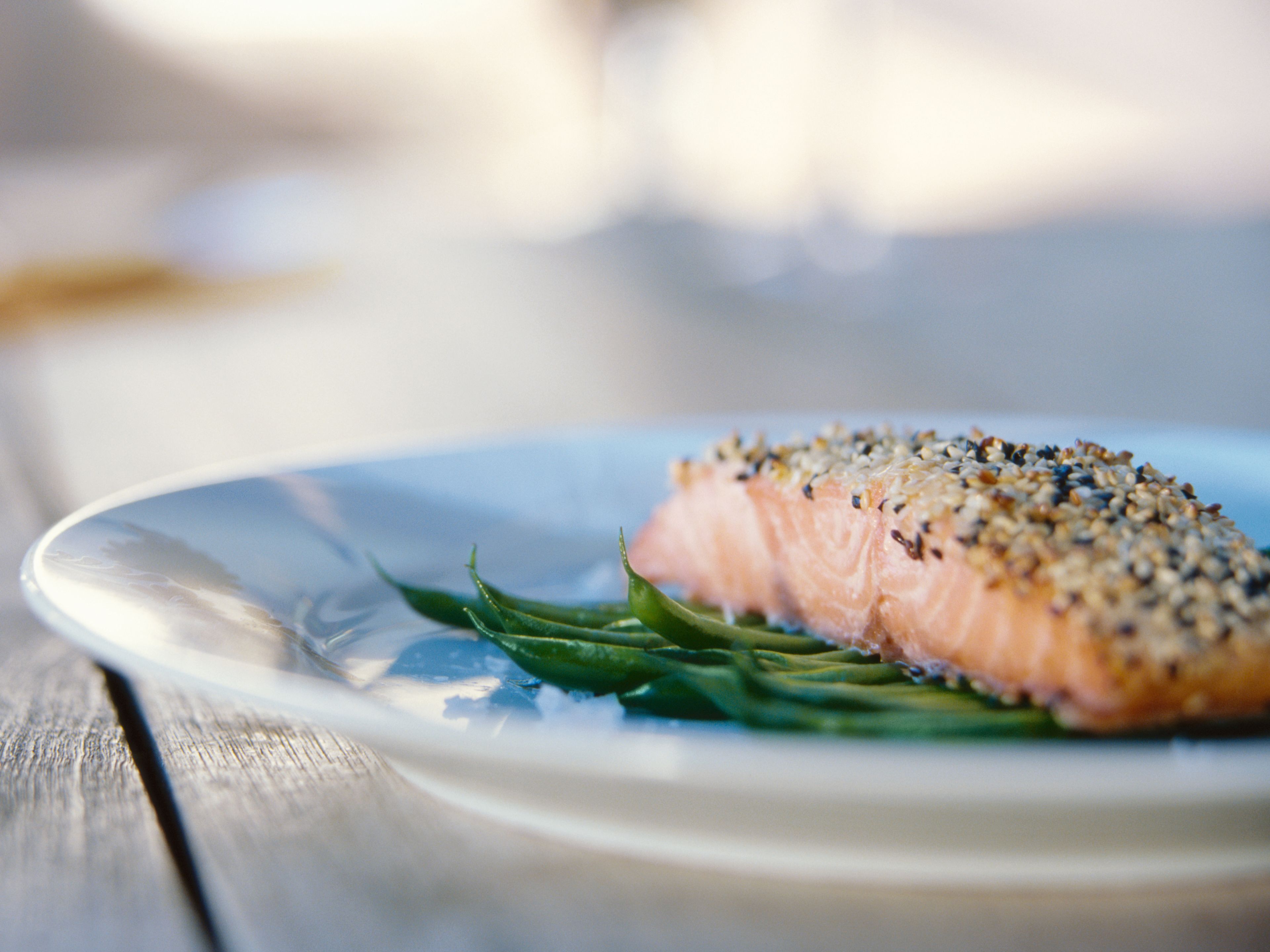 Salmon fillet with a sesame crust served on a bed of green vegetables on a white plate. Salmon fillet with a sesame crust served on a bed of green vegetables on a white plate.
