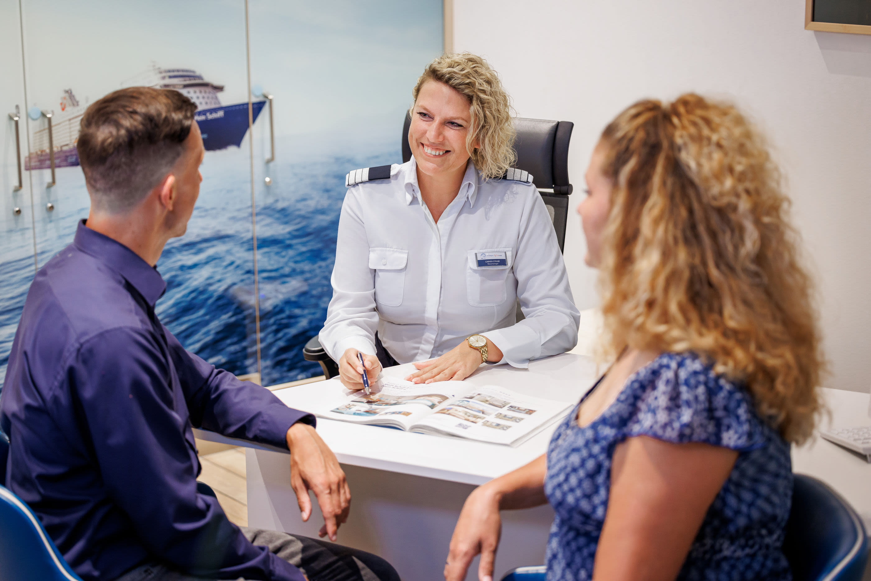 Drei Personen im Beratungsgespräch, Kreuzfahrtschiff der Mein Schiff® Flotte im Hintergrund.