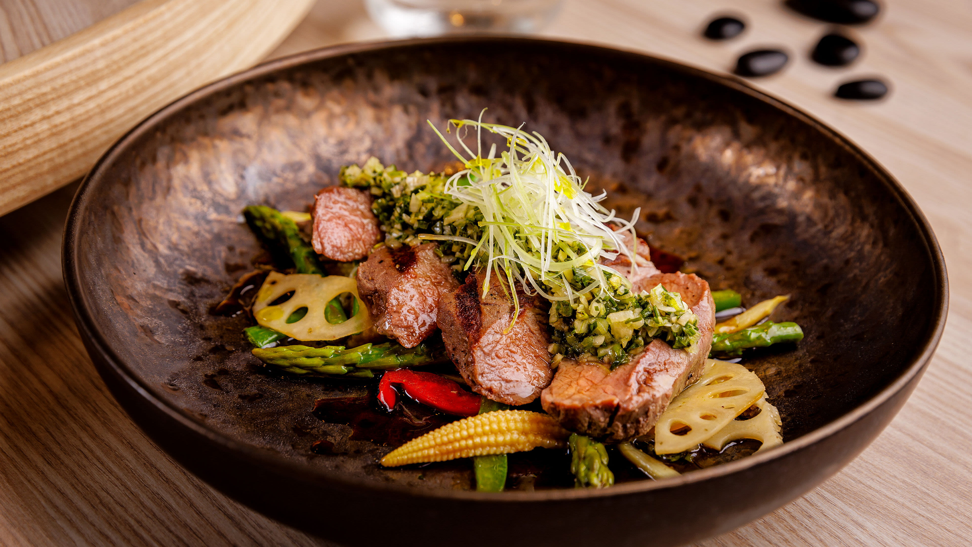 Gourmetgericht mit Fleisch, Gemüse und Kräutern in brauner Schale.