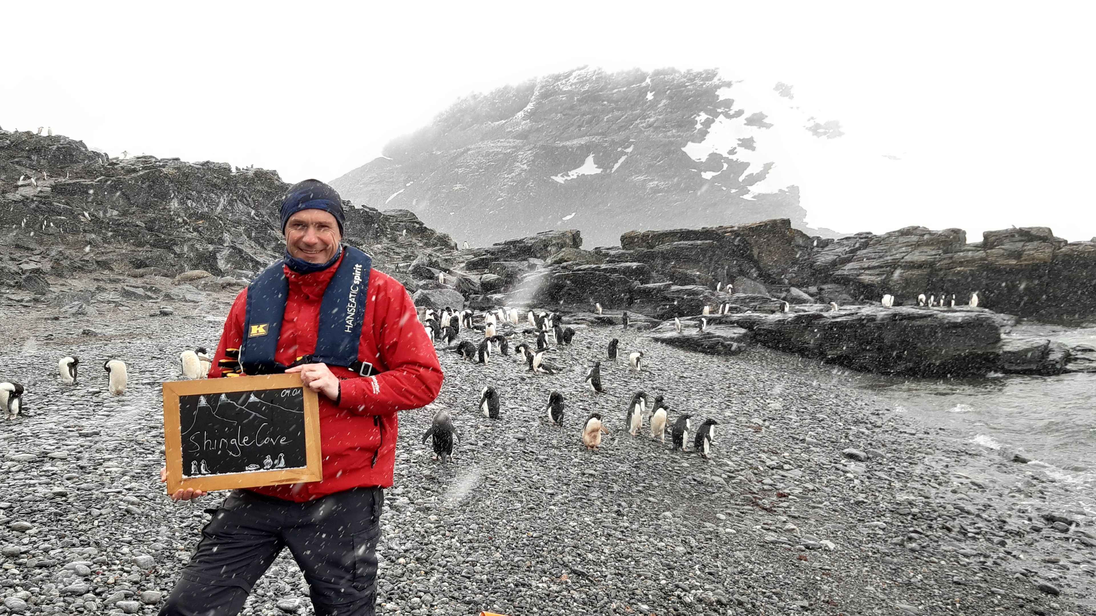 Mann in roter Jacke mit Pinguinen am verschneiten Strand von Shingle Cove. Mann in roter Jacke mit Pinguinen am verschneiten Strand von Shingle Cove.