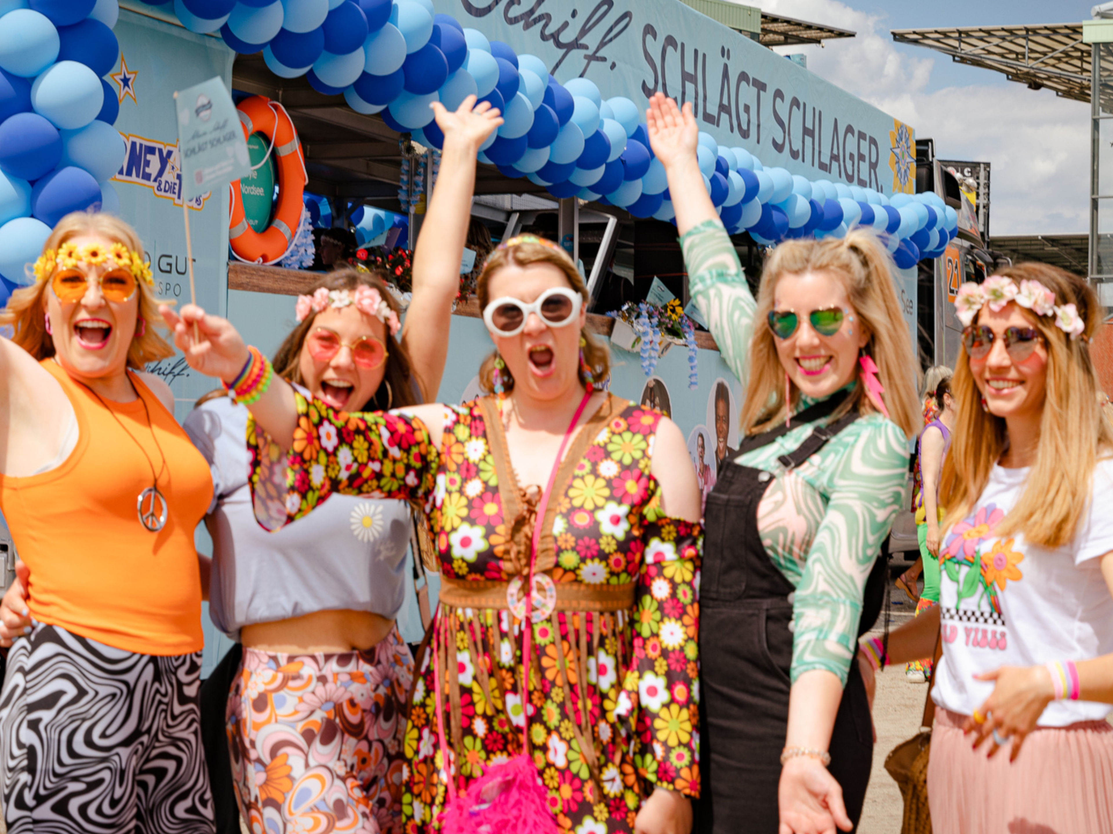 Gruppe fröhlicher Frauen in bunter Hippie-Kleidung vor geschmücktem Wagen. Gruppe fröhlicher Frauen in bunter Hippie-Kleidung vor geschmücktem Wagen.