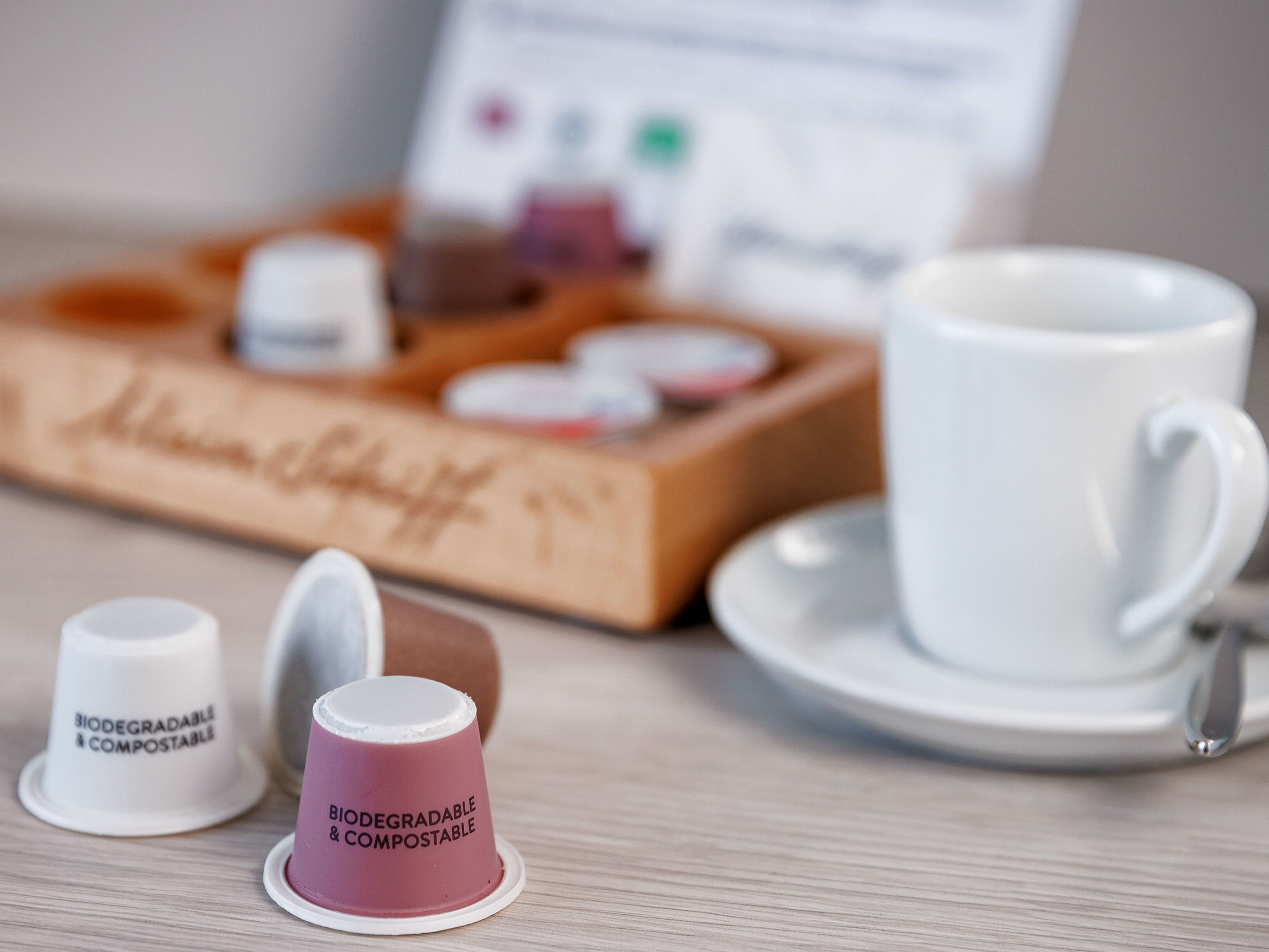 Biologisch abbaubare Kaffeekapseln und weiße Tasse auf Tisch. Biologisch abbaubare Kaffeekapseln und weiße Tasse auf Tisch.