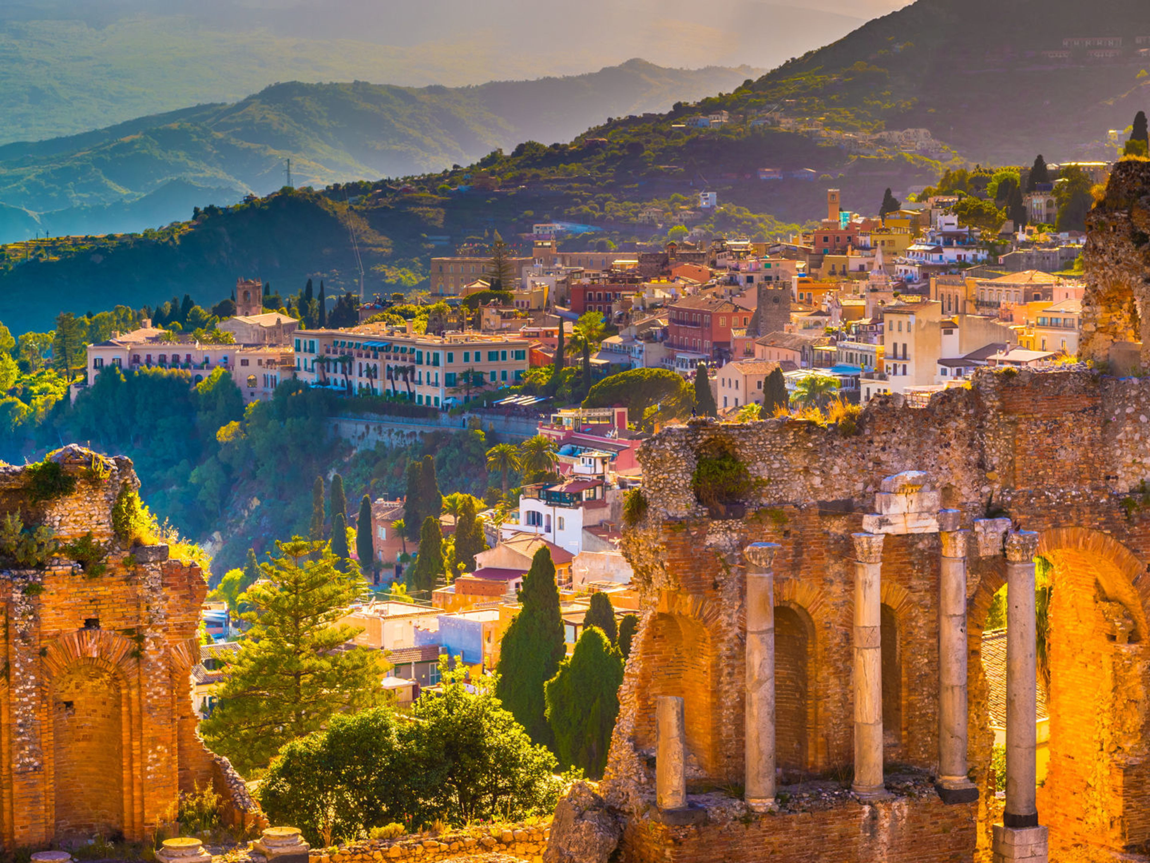 Antike Ruinen in Taormina, Sizilien, mit bunten Häusern und grünen Hügeln im Hintergrund. Antike Ruinen in Taormina, Sizilien, mit bunten Häusern und grünen Hügeln im Hintergrund.