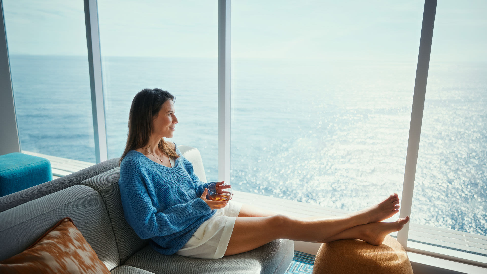 Frau in blauem Pullover entspannt auf Sofa, Meerblick. Frau in blauem Pullover entspannt auf Sofa, Meerblick.
